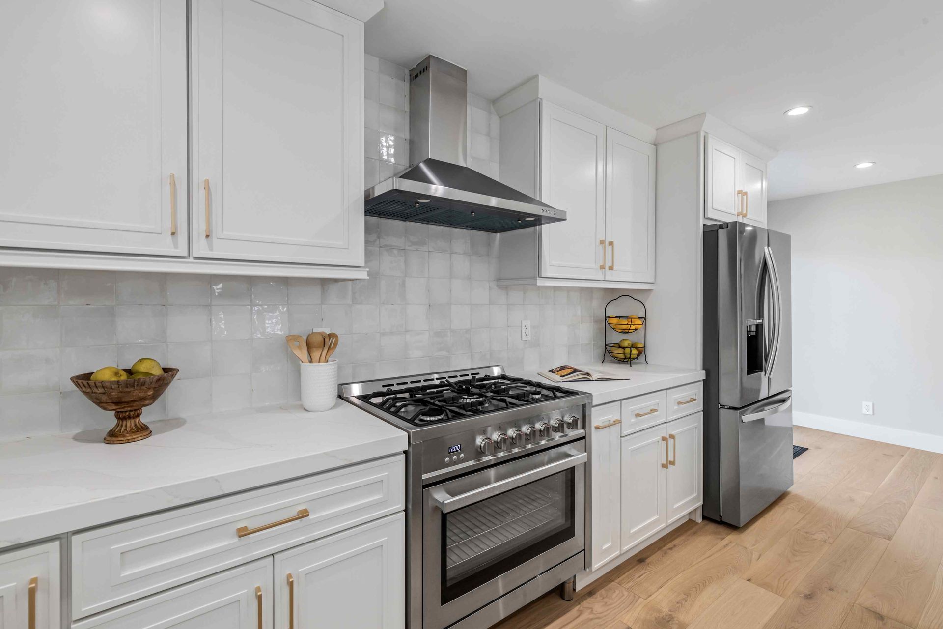 White kitchen with stainless steel appliances, light cabinets, and marble tile backsplash.