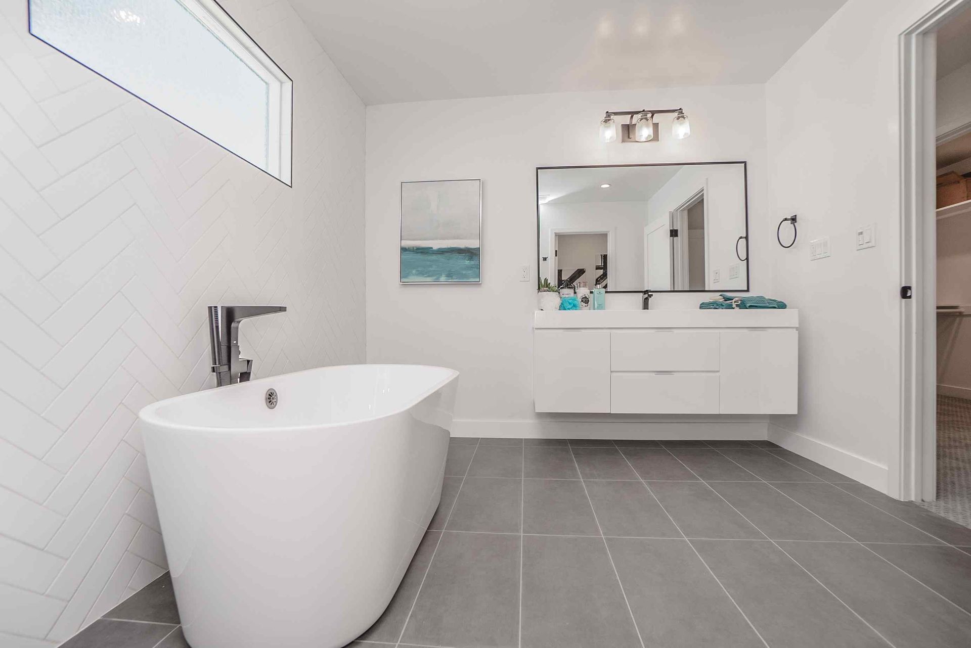 Modern white bathroom with gray tile floor, soaking tub, and floating vanity.