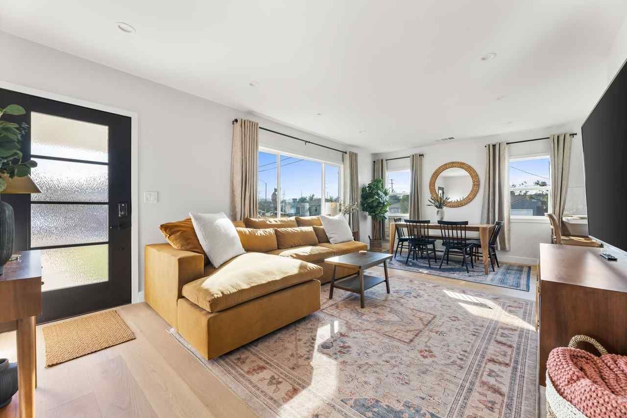 Bright living room with mustard sectional, large windows, and a dining table.