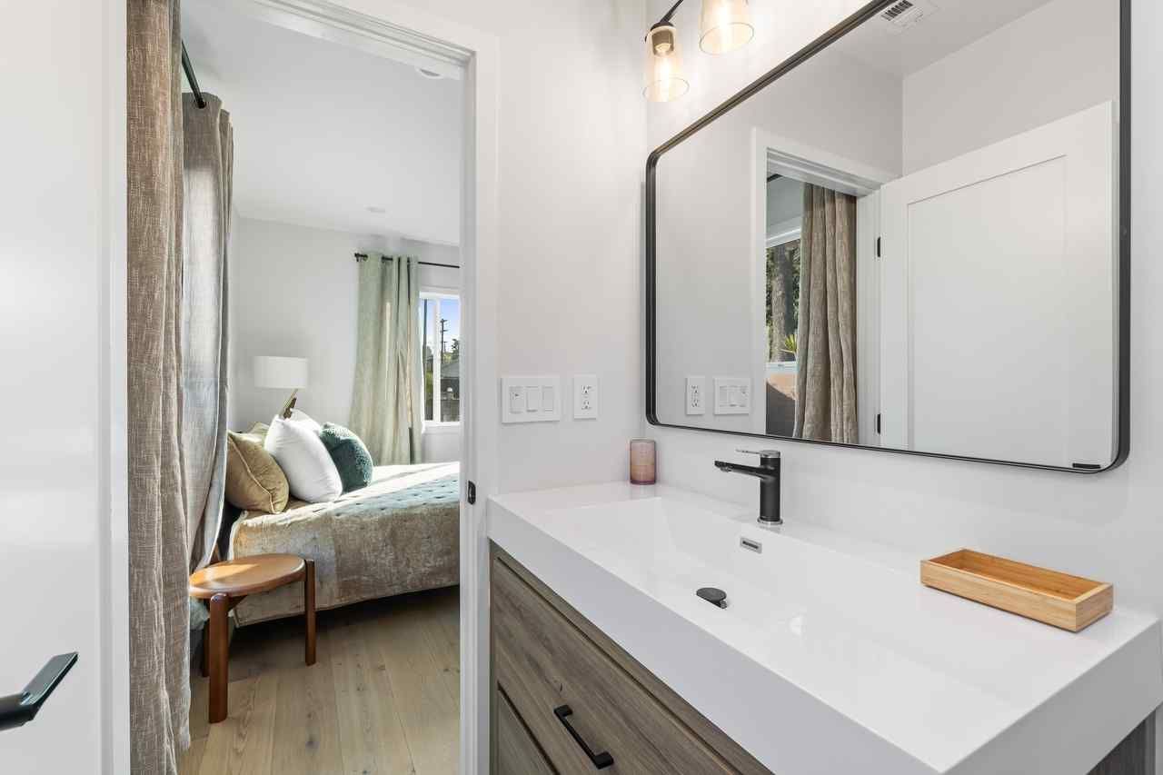 Bathroom with white sink, mirror, and open door to bedroom with bed.