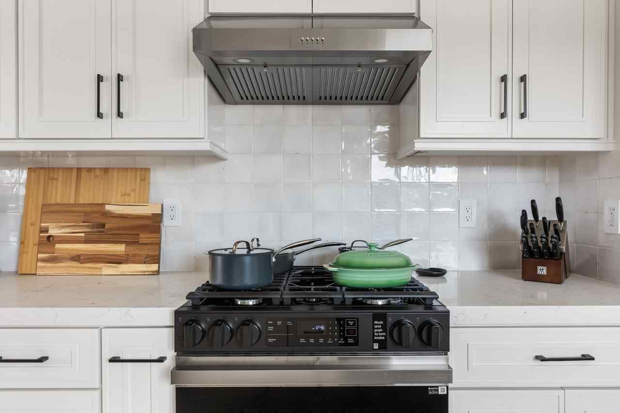 A kitchen with white cabinets, a gas stove with two pots, and a stainless steel range hood.