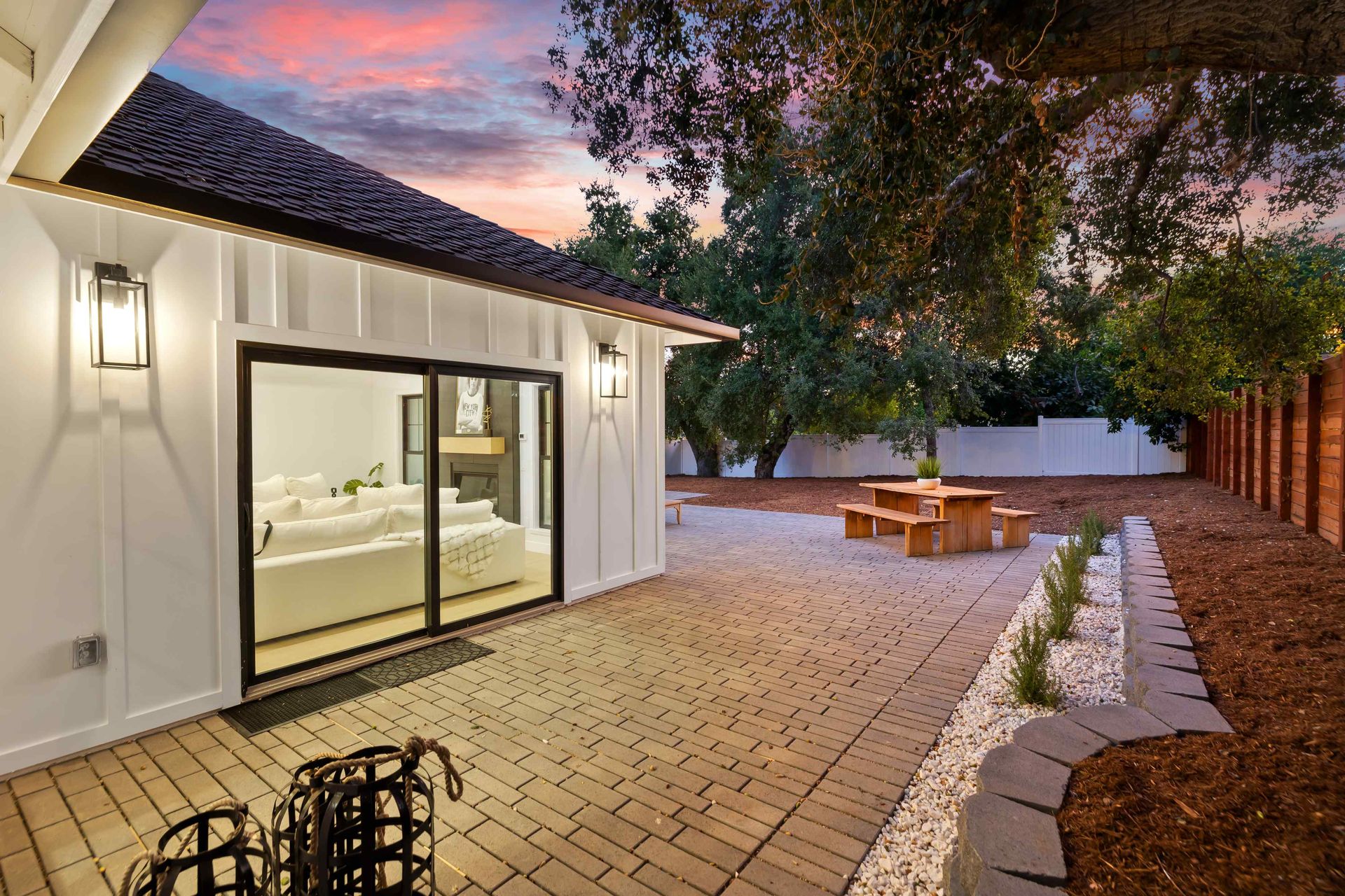 Backyard patio with white siding, black-framed sliding door, and wooden picnic table, under a twilight sky.