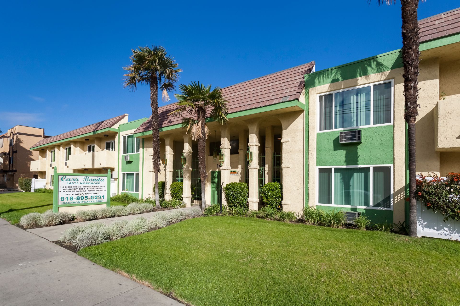 A green and tan apartment building with palm trees in front of it