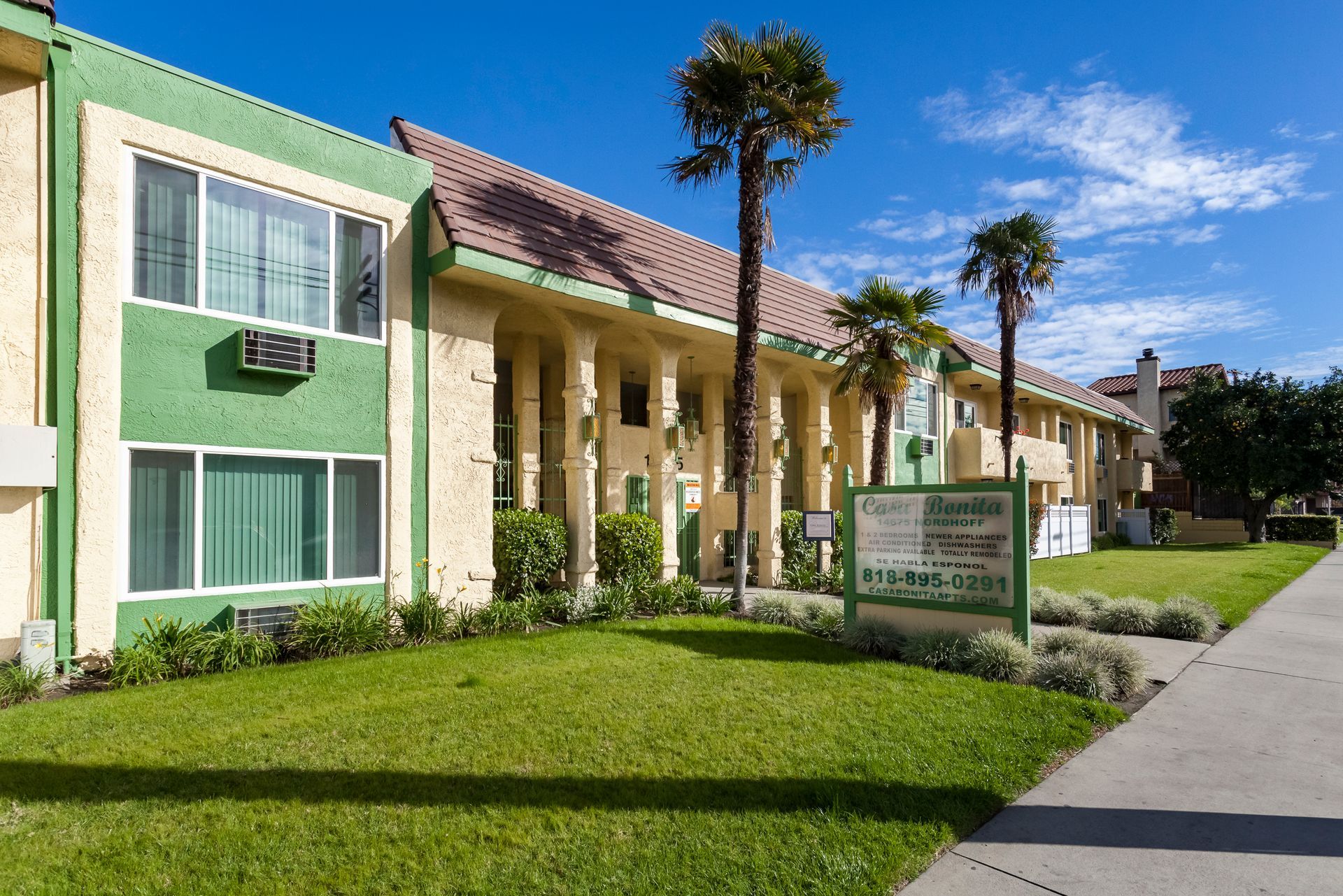 A green and tan apartment building with palm trees in front of it