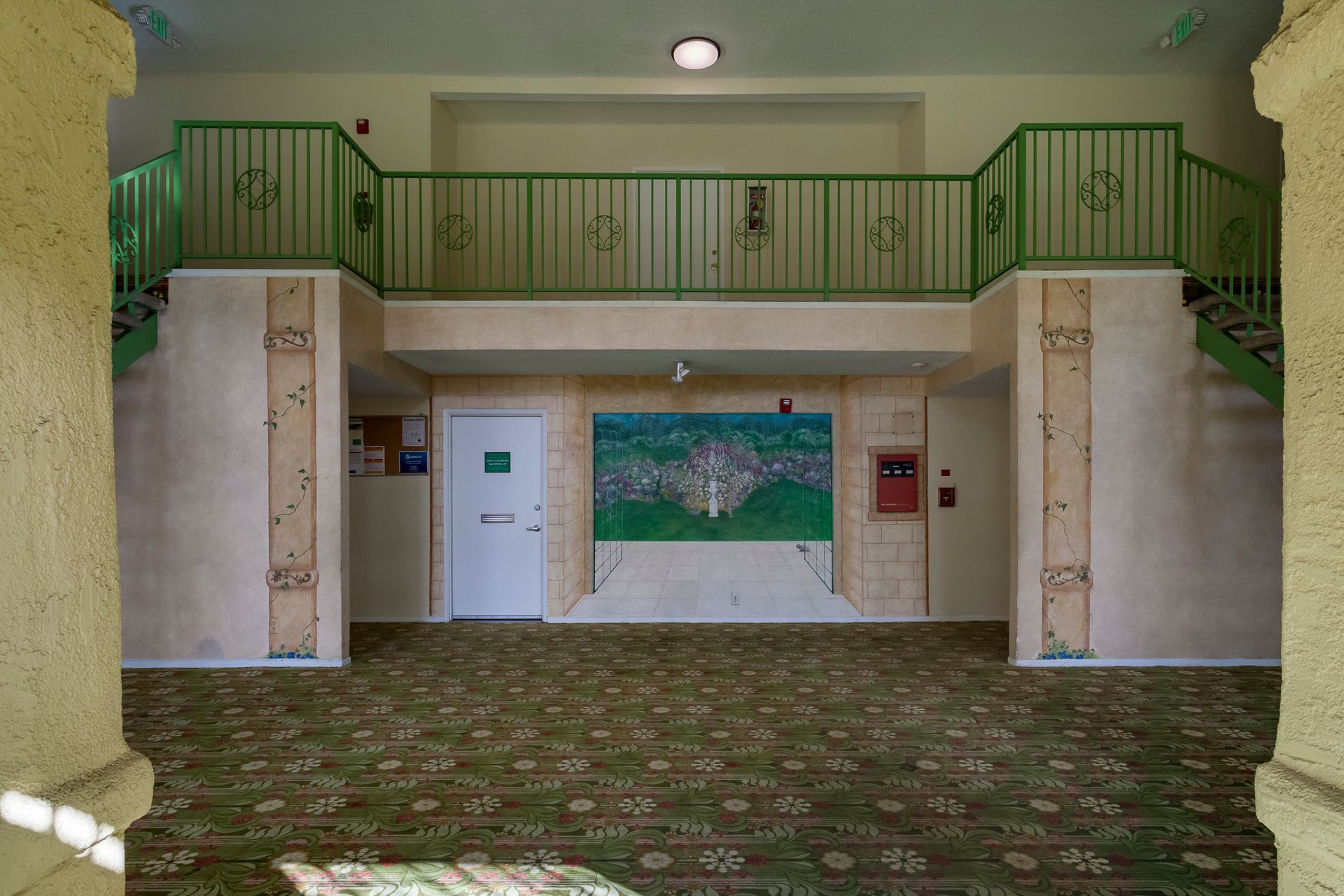 A hallway with a green railing and a painting on the wall