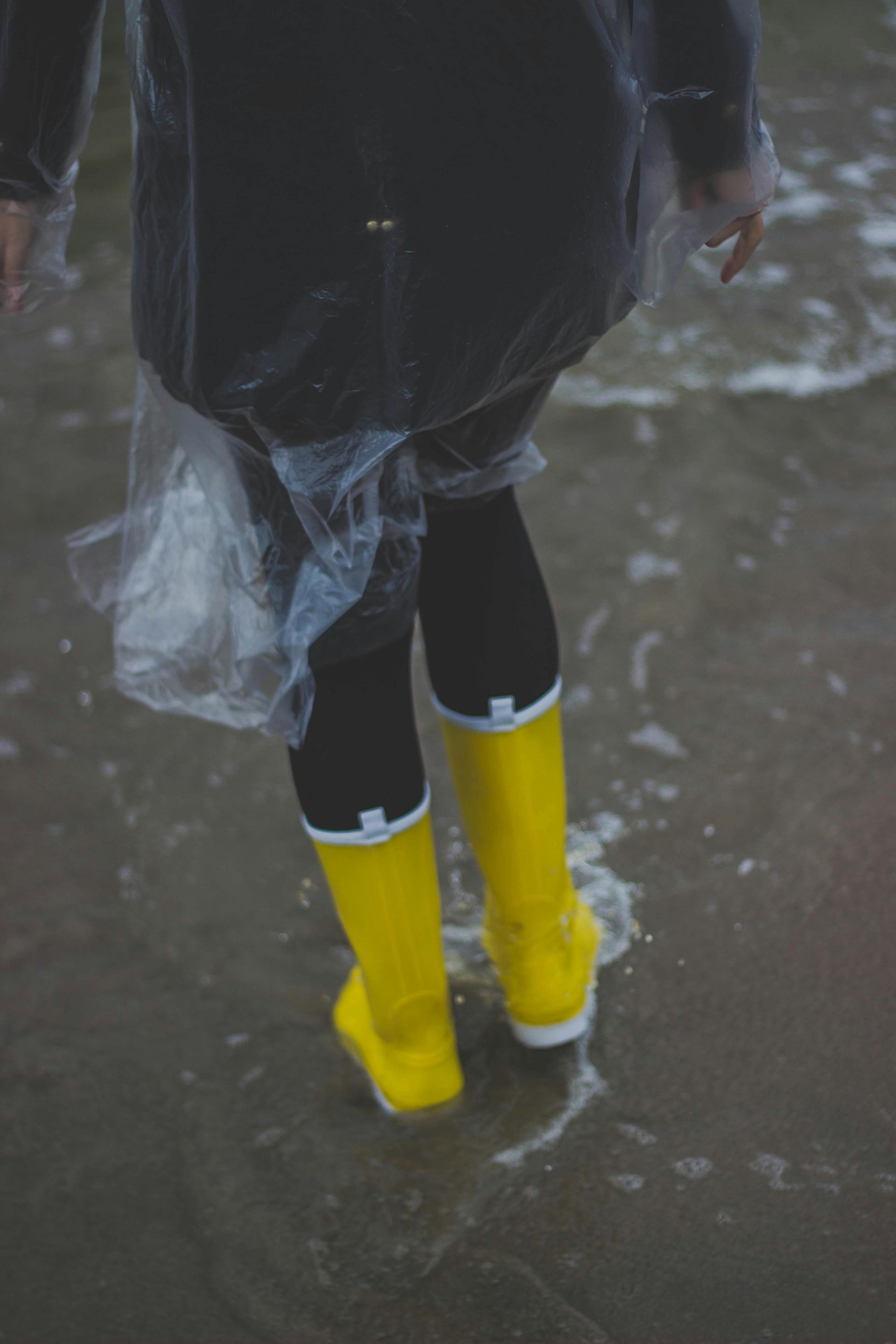 A person wearing yellow rain boots and a plastic poncho is walking in the water.