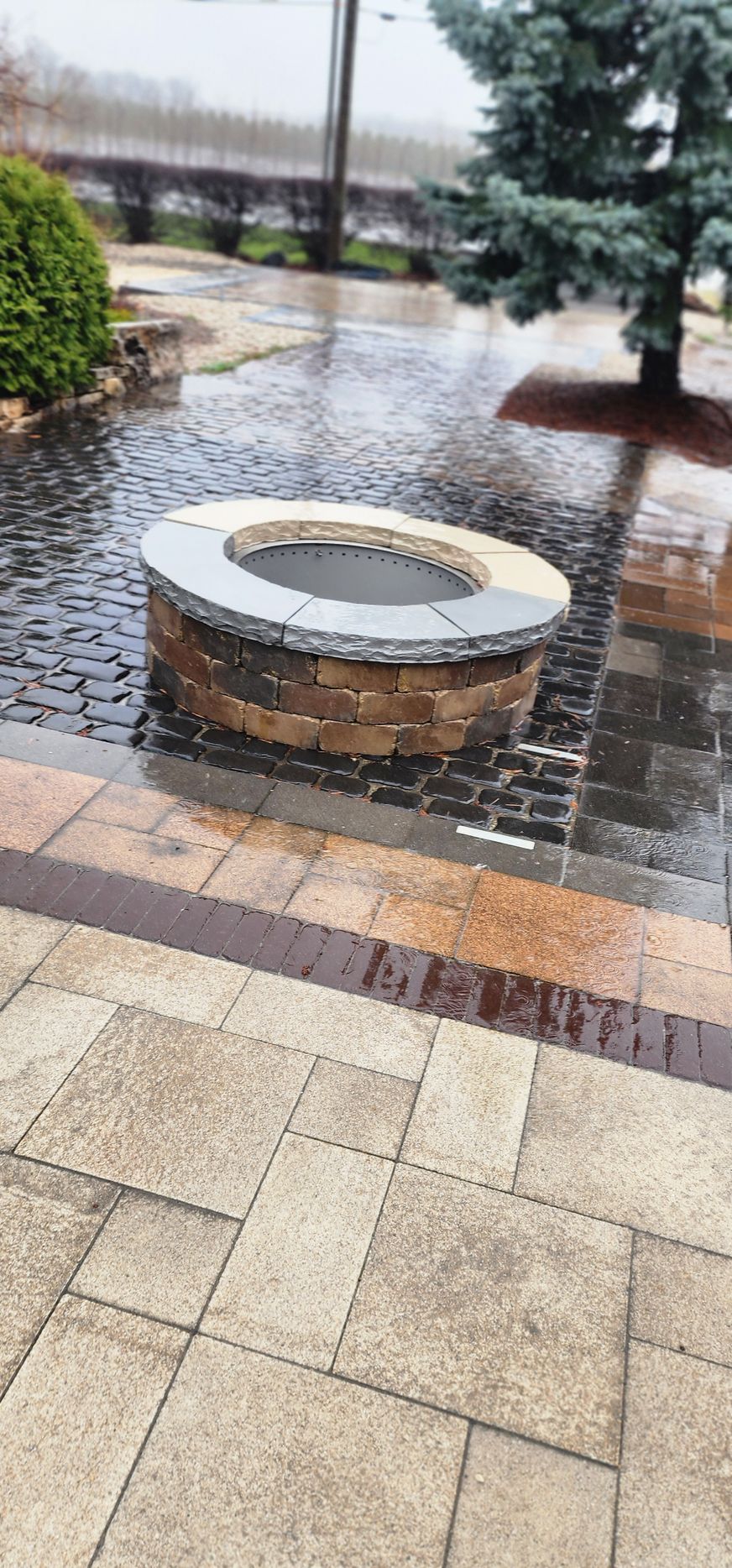 Fire pit made of stone with wet brick paving in an outdoor setting.