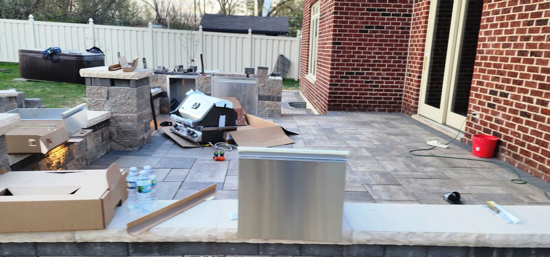 Backyard patio with an outdoor kitchen under construction; brick house.