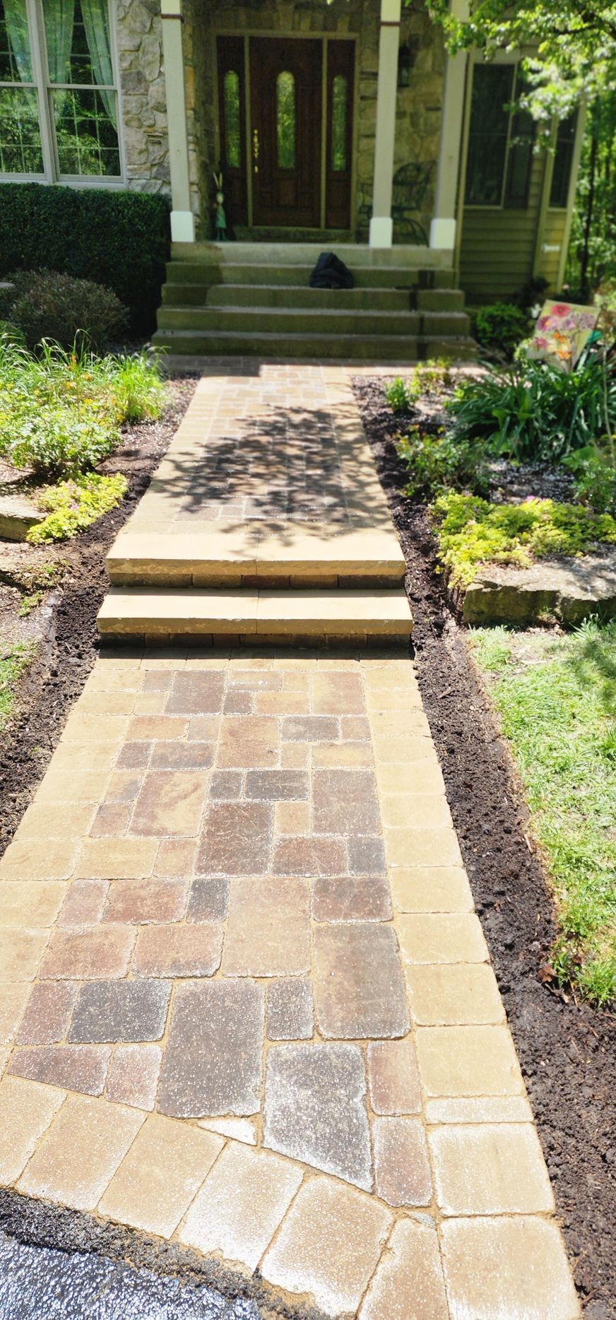 Stone walkway leading to a house with steps and a dark wooden door; landscaping on either side.