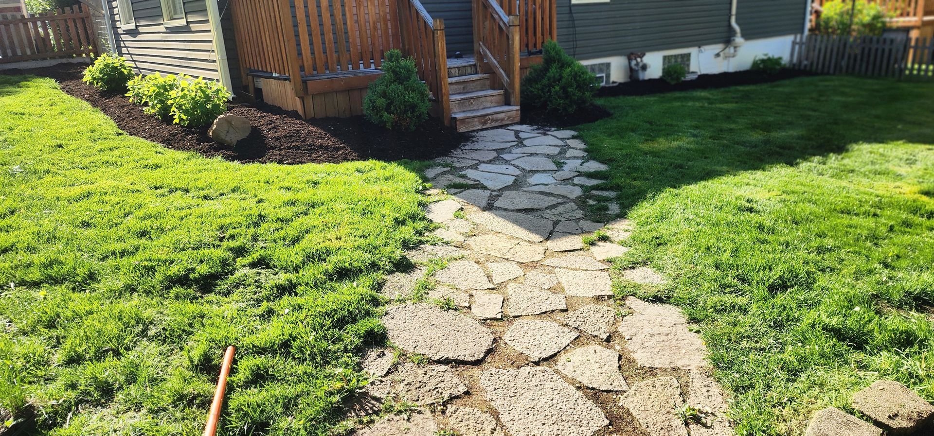 Stone path leading to wooden steps, surrounded by green grass and landscaping, sunlight.