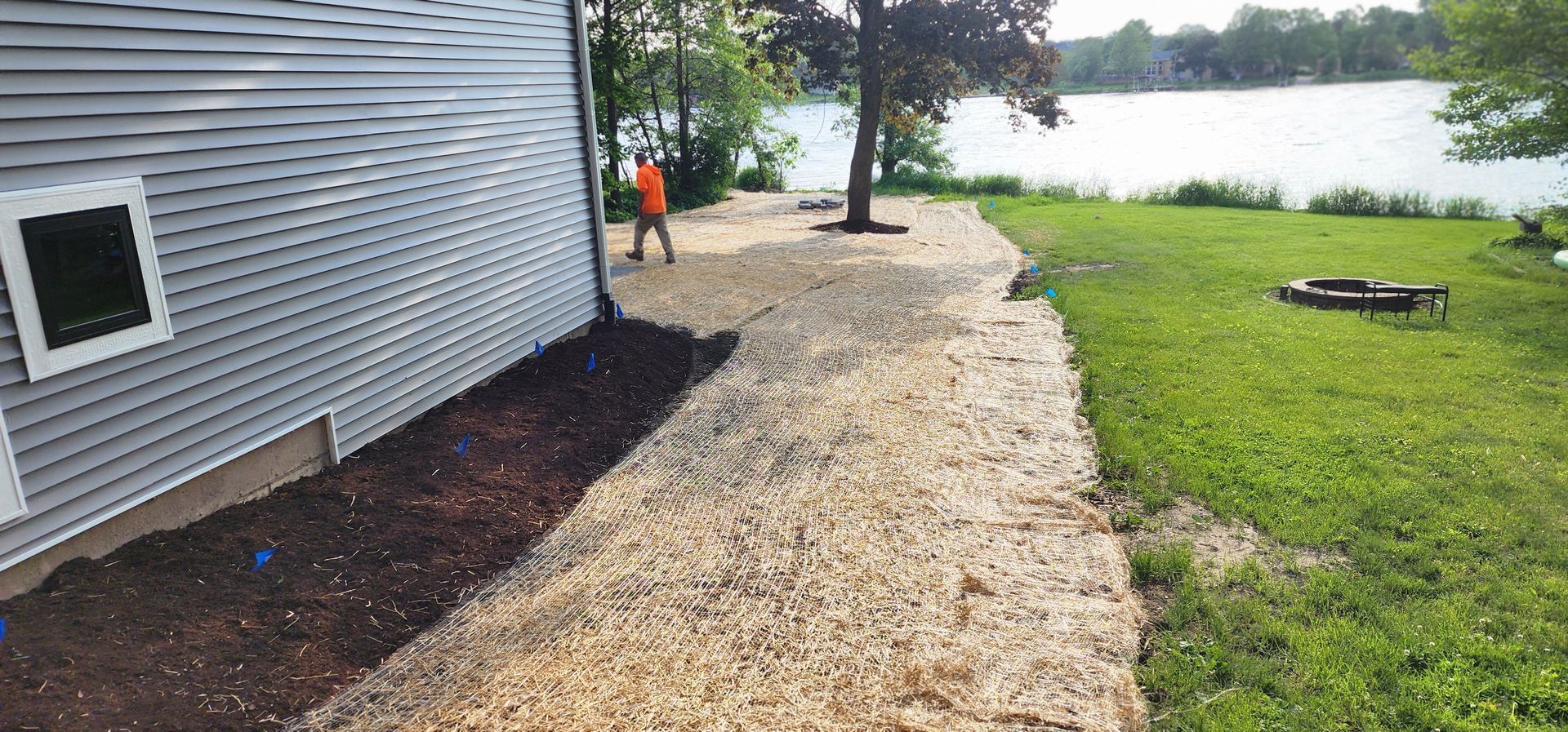 Side of a house with gravel path leading to a lake. A person in orange walks along the path.