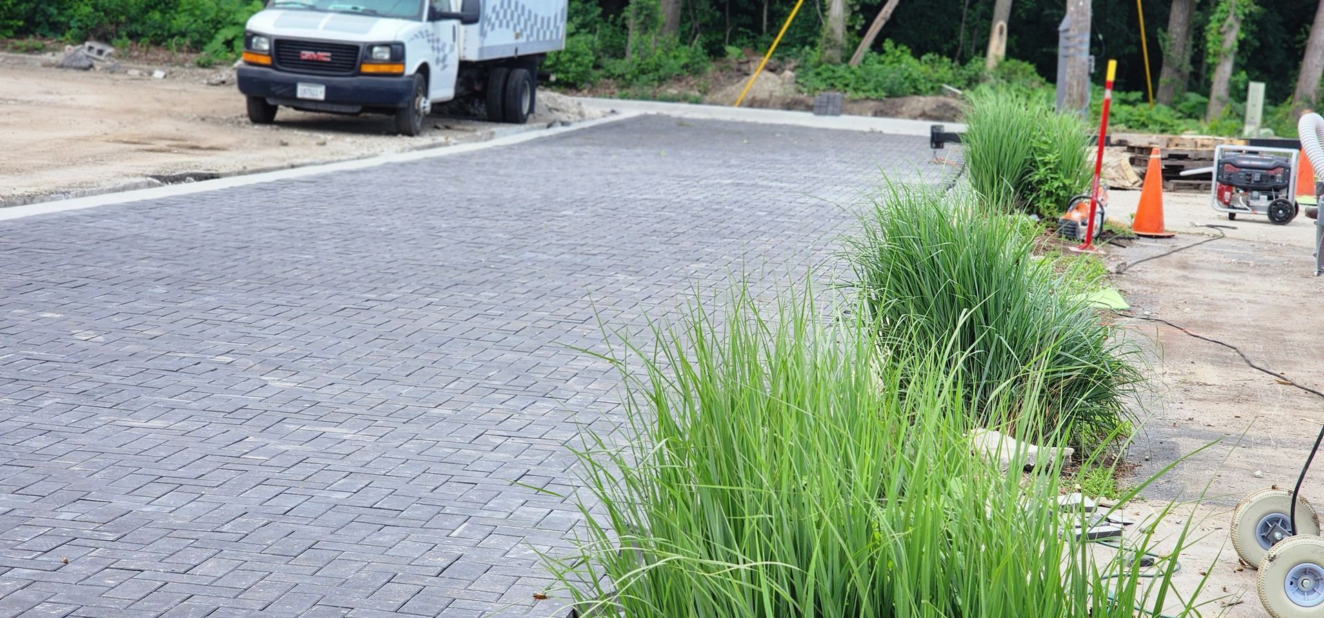 A truck parked on a cobblestone road, with overgrown grass in the foreground and construction equipment on the side.