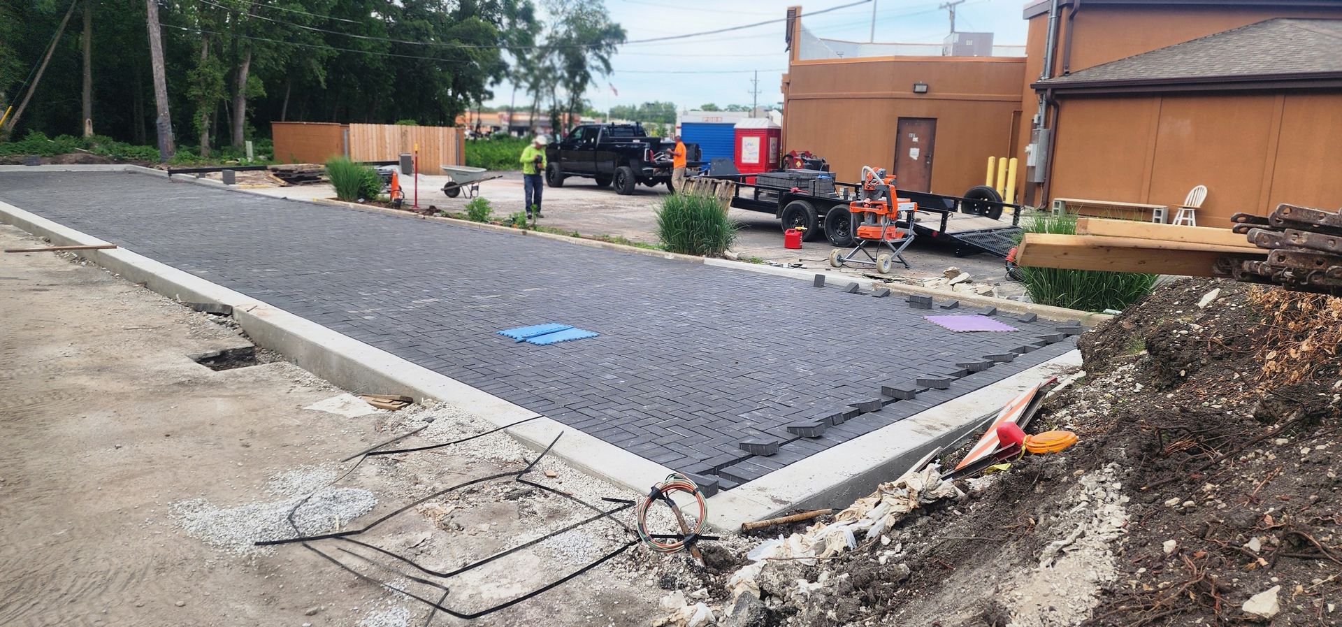 Construction site with a new paved area, concrete borders, and equipment near a building.