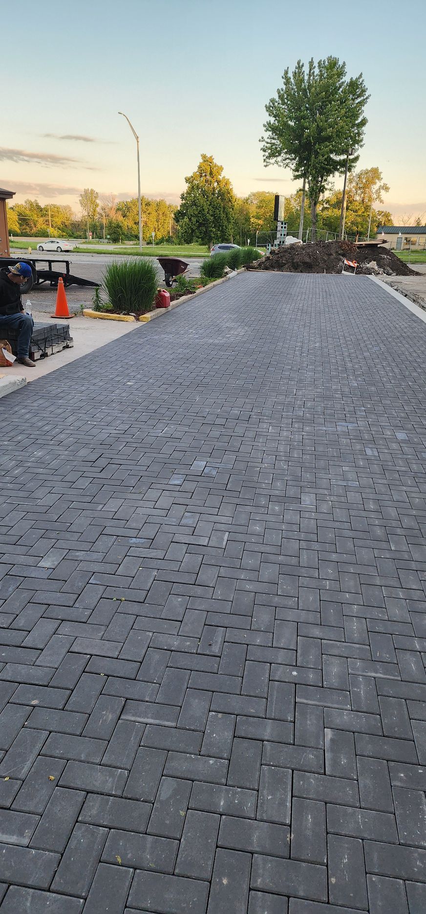 Brick driveway leads to a tree and landscaping in an outdoor setting.