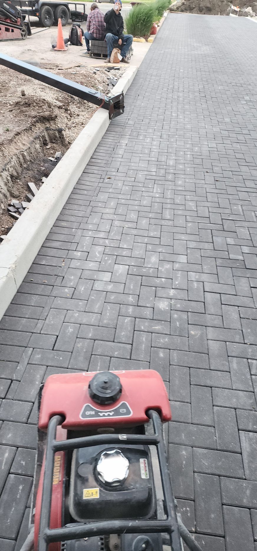 Construction workers installing brick pavers using a compactor.