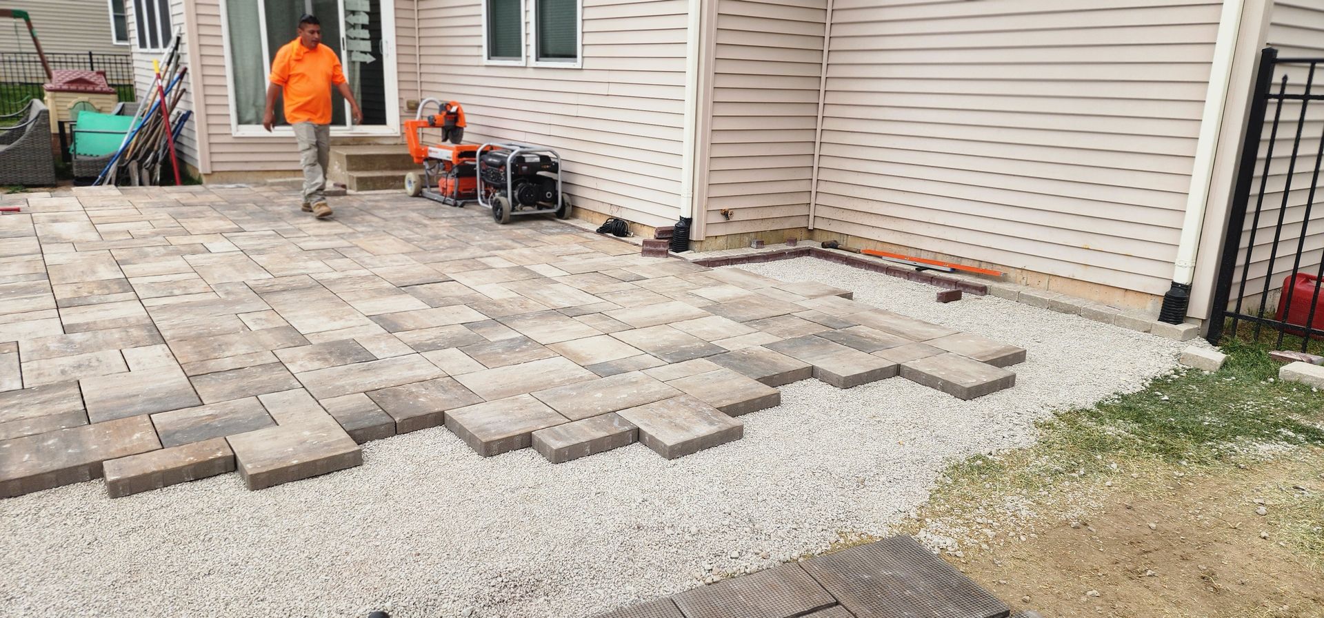 Man laying pavers on a gravel base for a patio near a house.