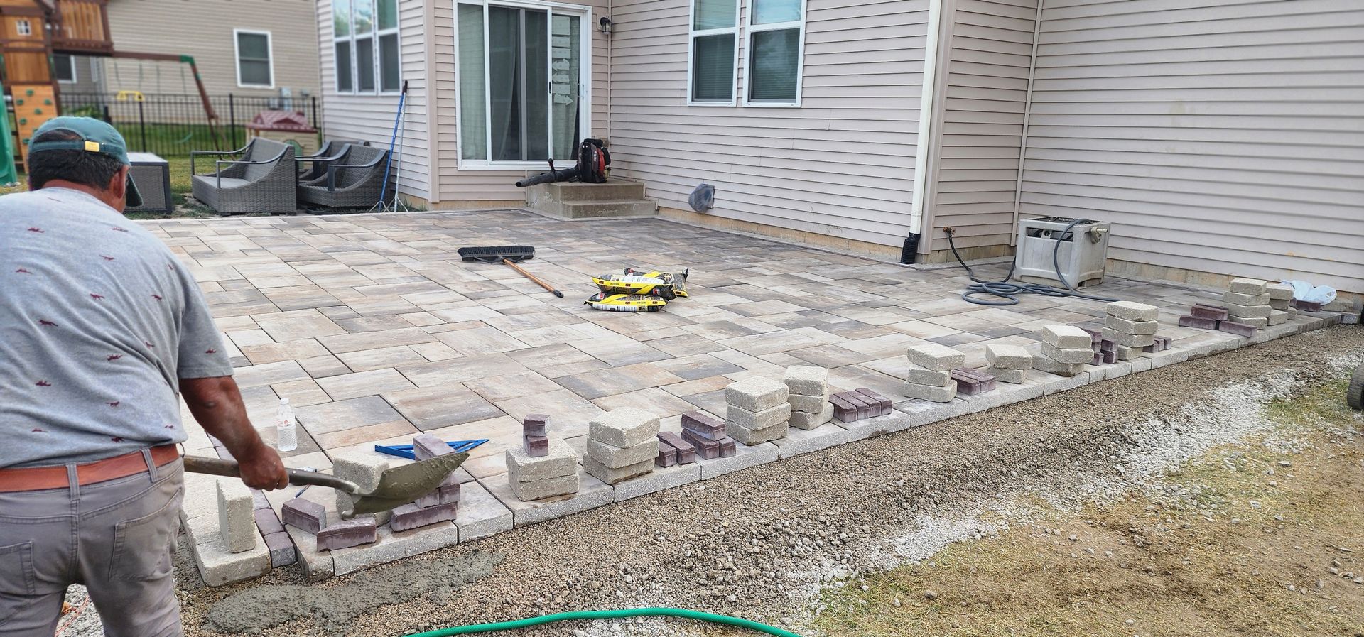 Man laying pavers for a patio near a house, using a shovel.