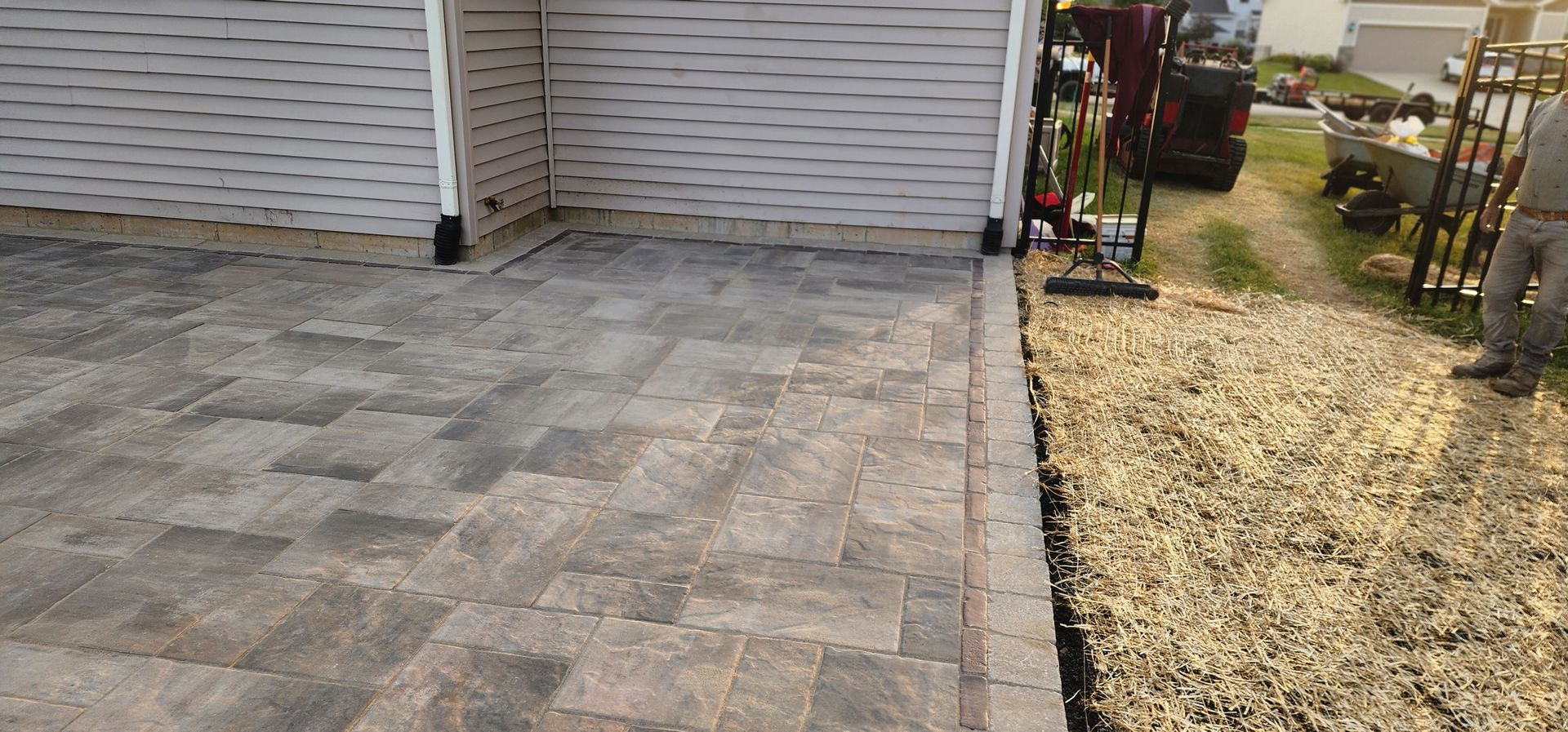 A paved patio next to a gravel area, beside a house with white siding.