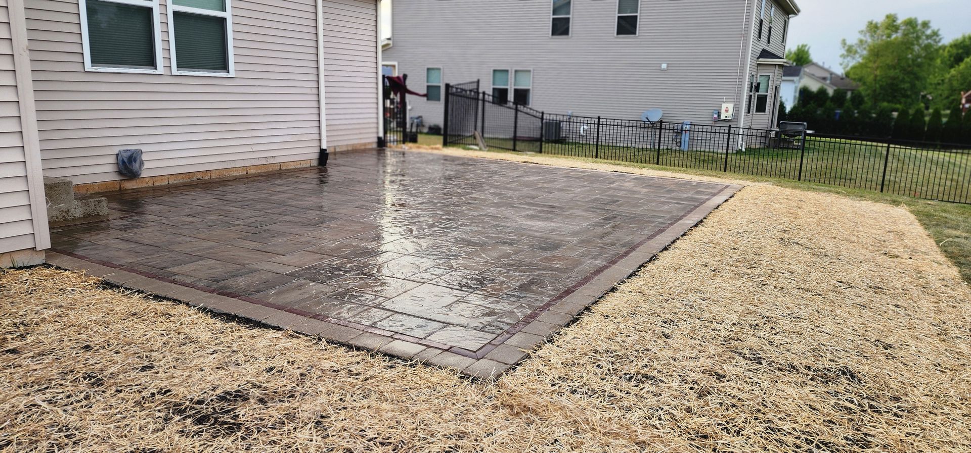 A concrete patio surrounded by gravel, next to a house with a fence in the background.