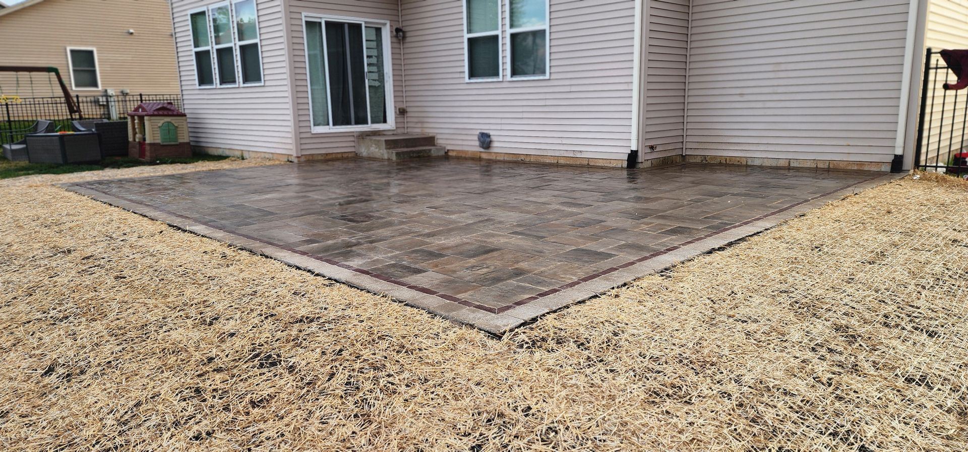 A concrete patio bordered by gravel in a backyard next to a beige house with windows and a sliding glass door.