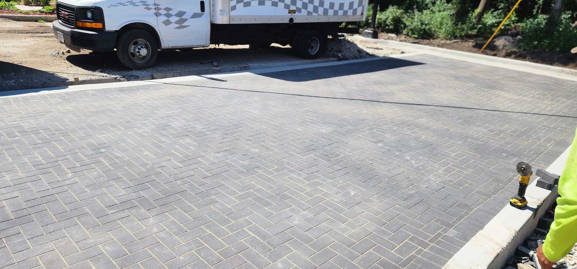 A white truck parked on a paved driveway; a person in a lime green shirt stands nearby with a drill.