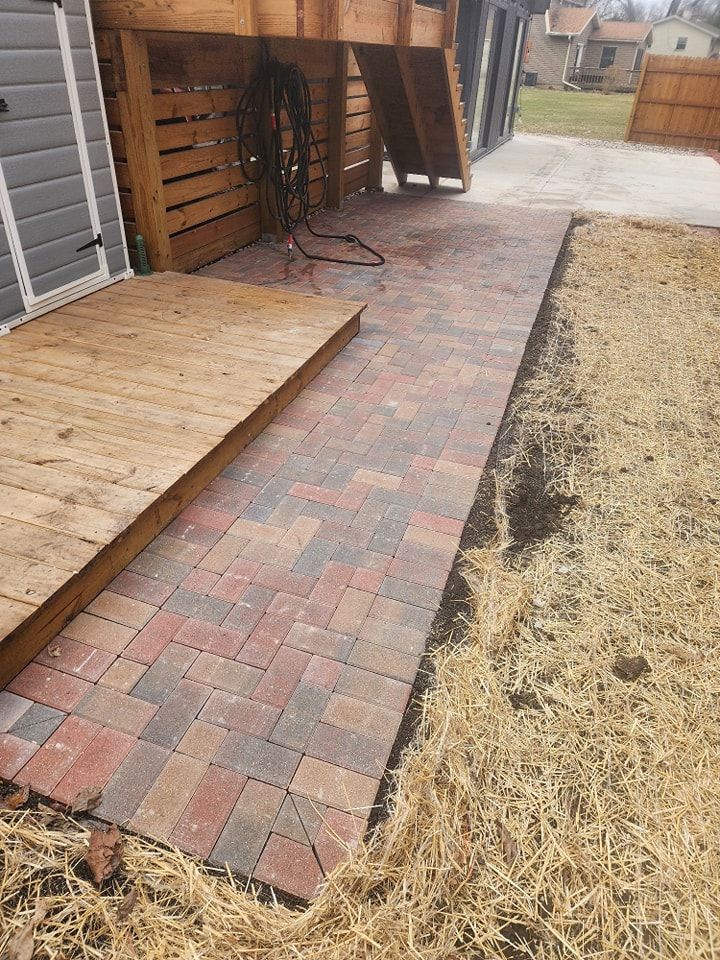 Brick pathway beside a wooden deck and a patch of dry grass, leading from a building.