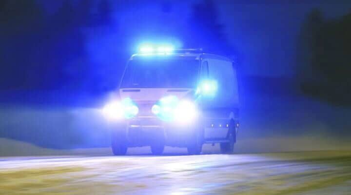 Vehículo de emergencia, faros y luces azules encendidas, circulando por una carretera de noche.