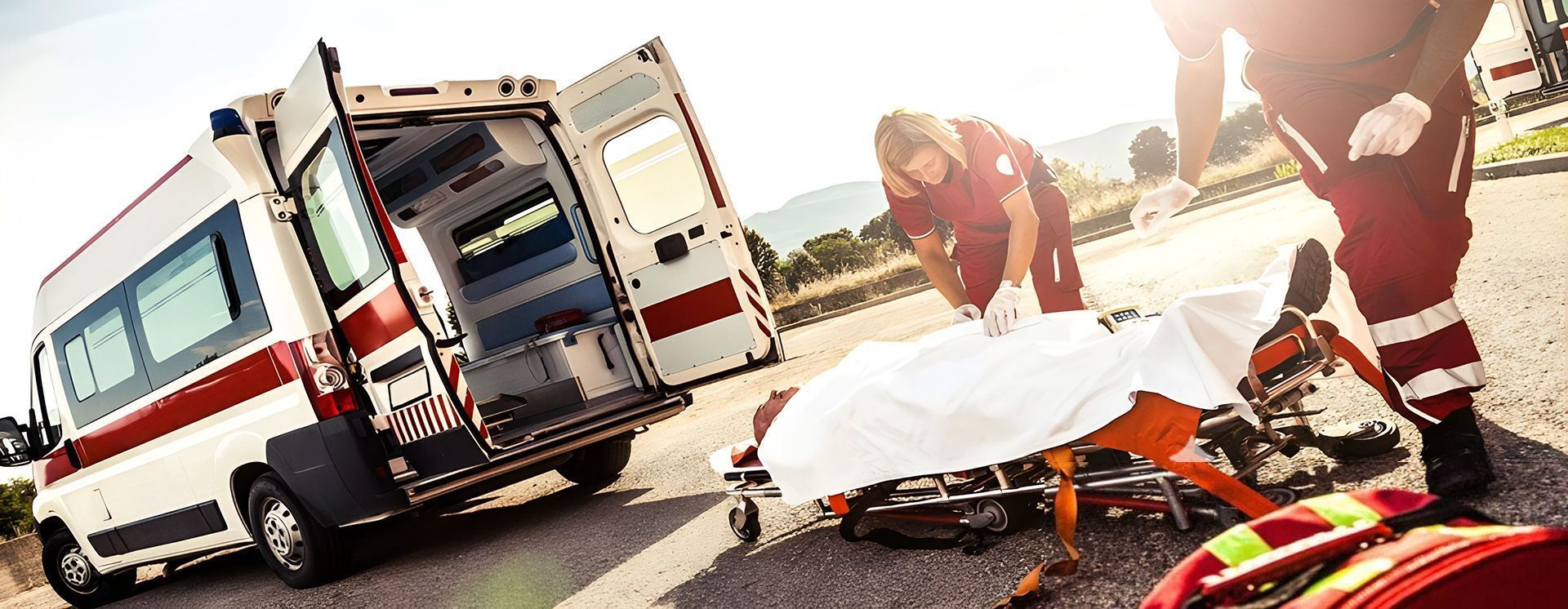 Ambulancia con las puertas traseras abiertas. Médicos atienden a una persona en camilla en la carretera.