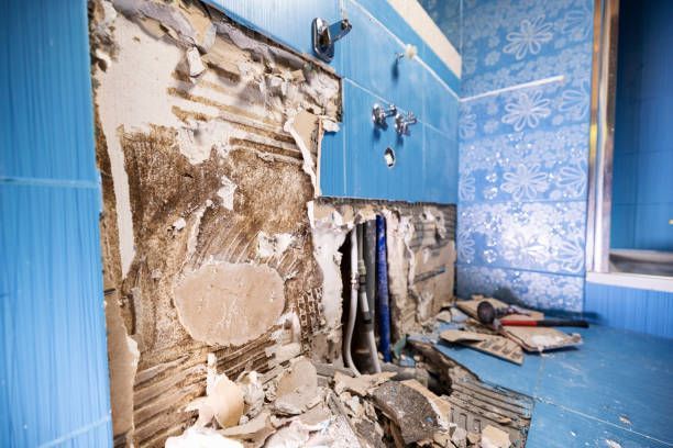 Water damaged bathroom wall with stripped tiles and exposed plumbing.
