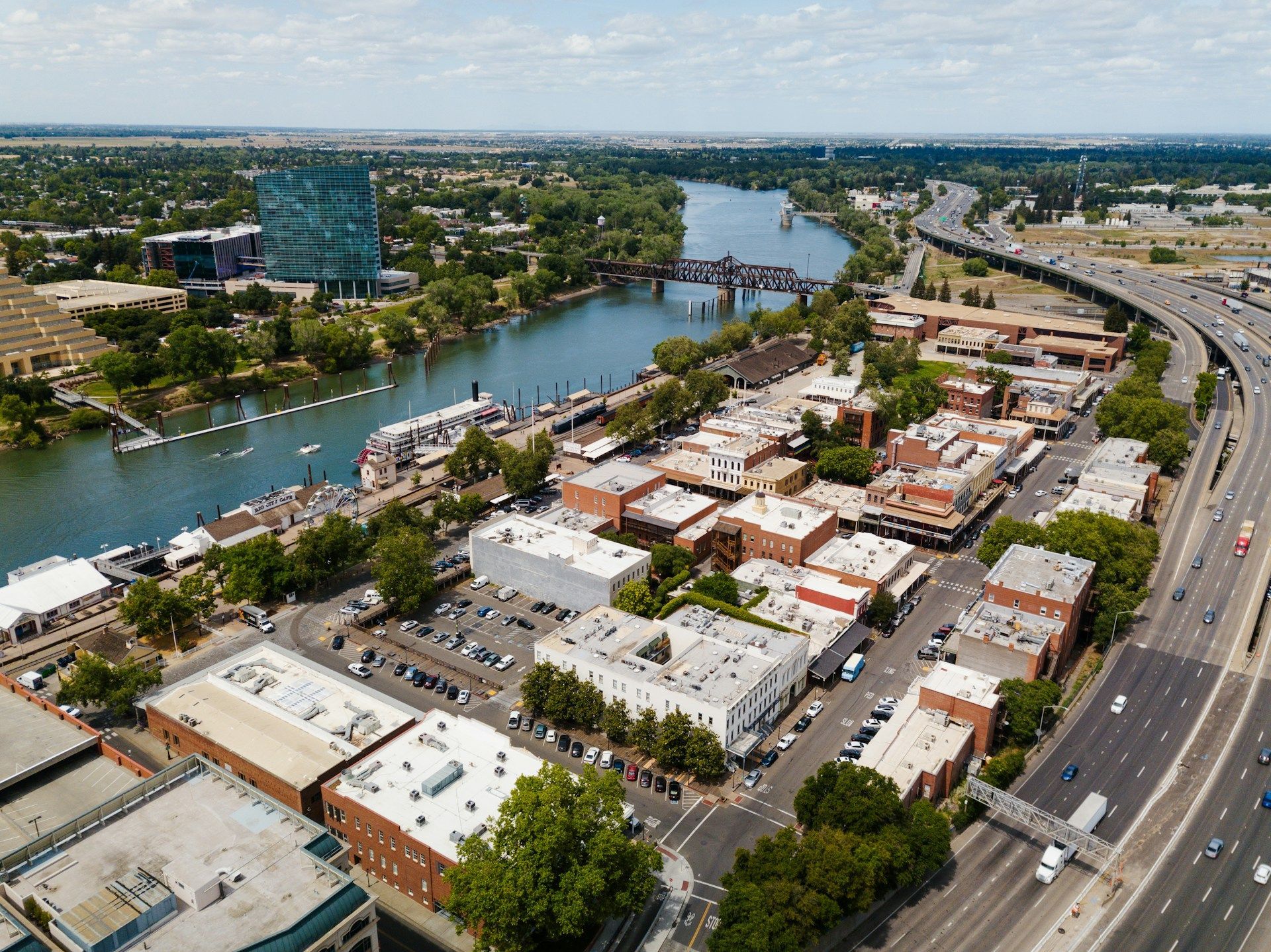 Aerial view of a city with a river, shops, and a highway. Bright sunny day with blue sky.