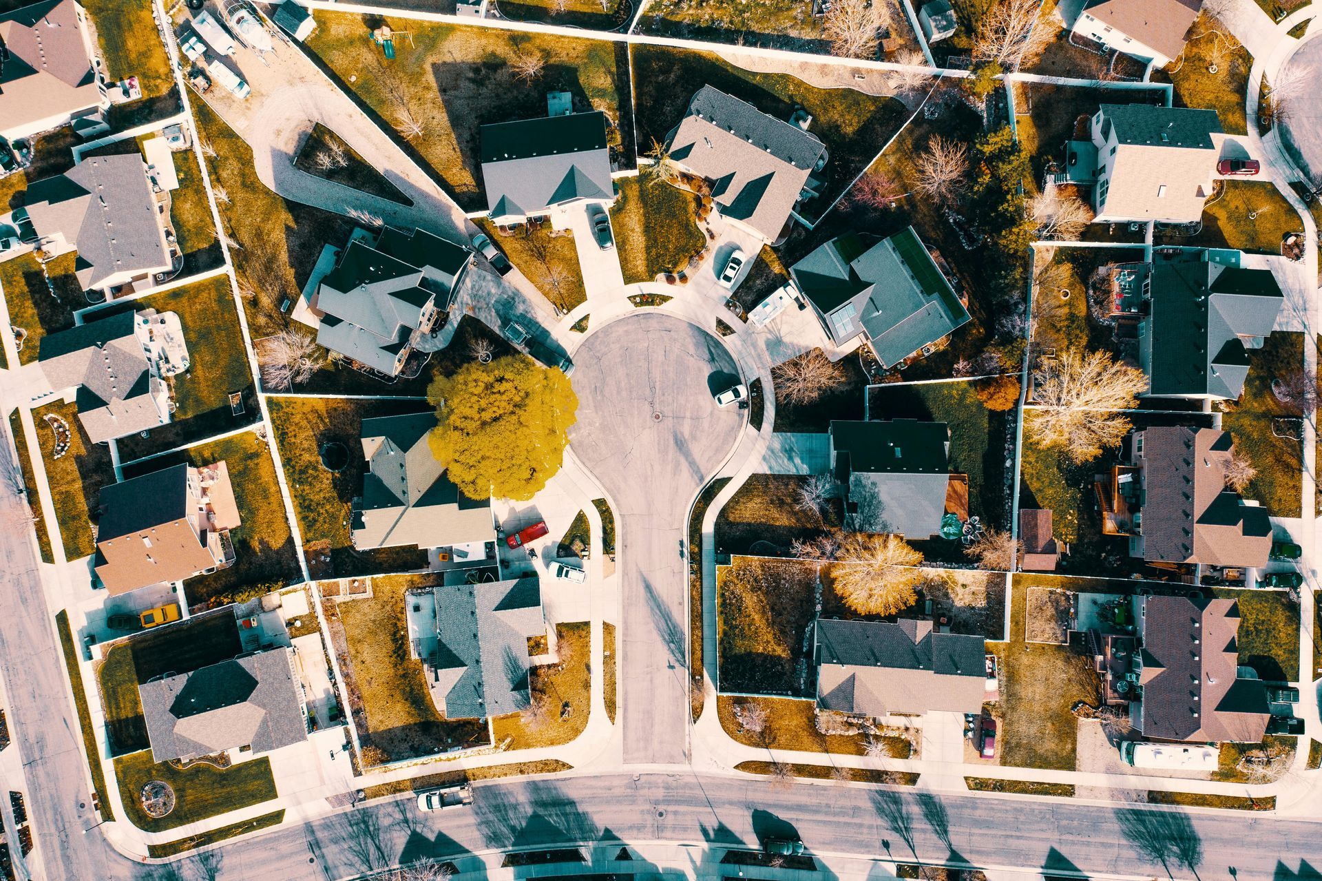 Aerial view of a suburban neighborhood with houses surrounding a circular road; tan yards, gray rooftops.