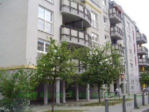Ein großes Mehrfamilienhaus mit Balkonen und Bäumen davor.