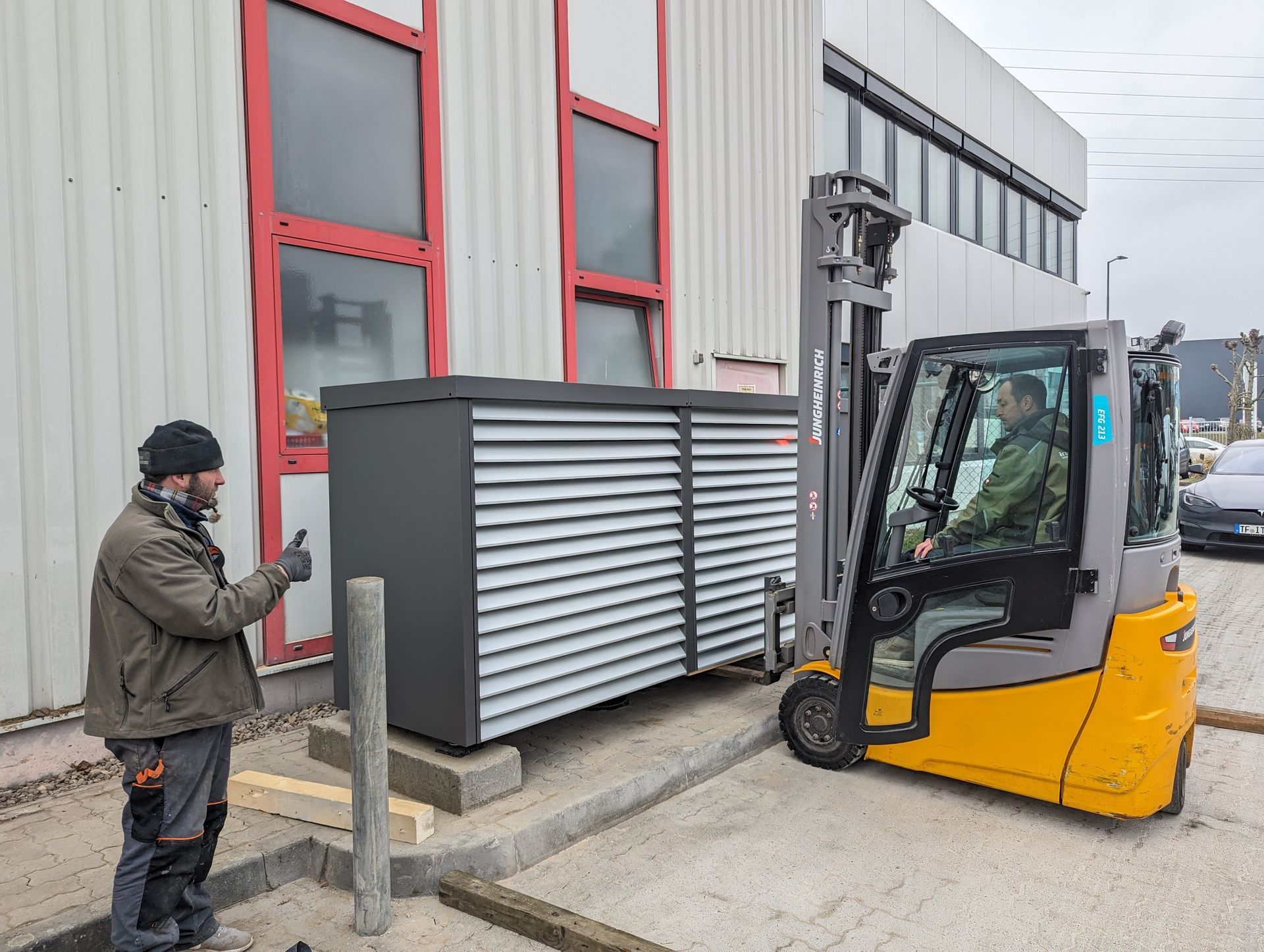 Ein Mann steht neben einem Gabelstapler, auf dem eine Wärmepumpe ist