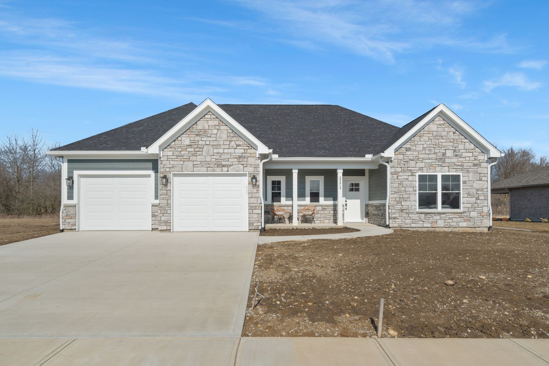 A large stone house with a white garage door and a concrete driveway.