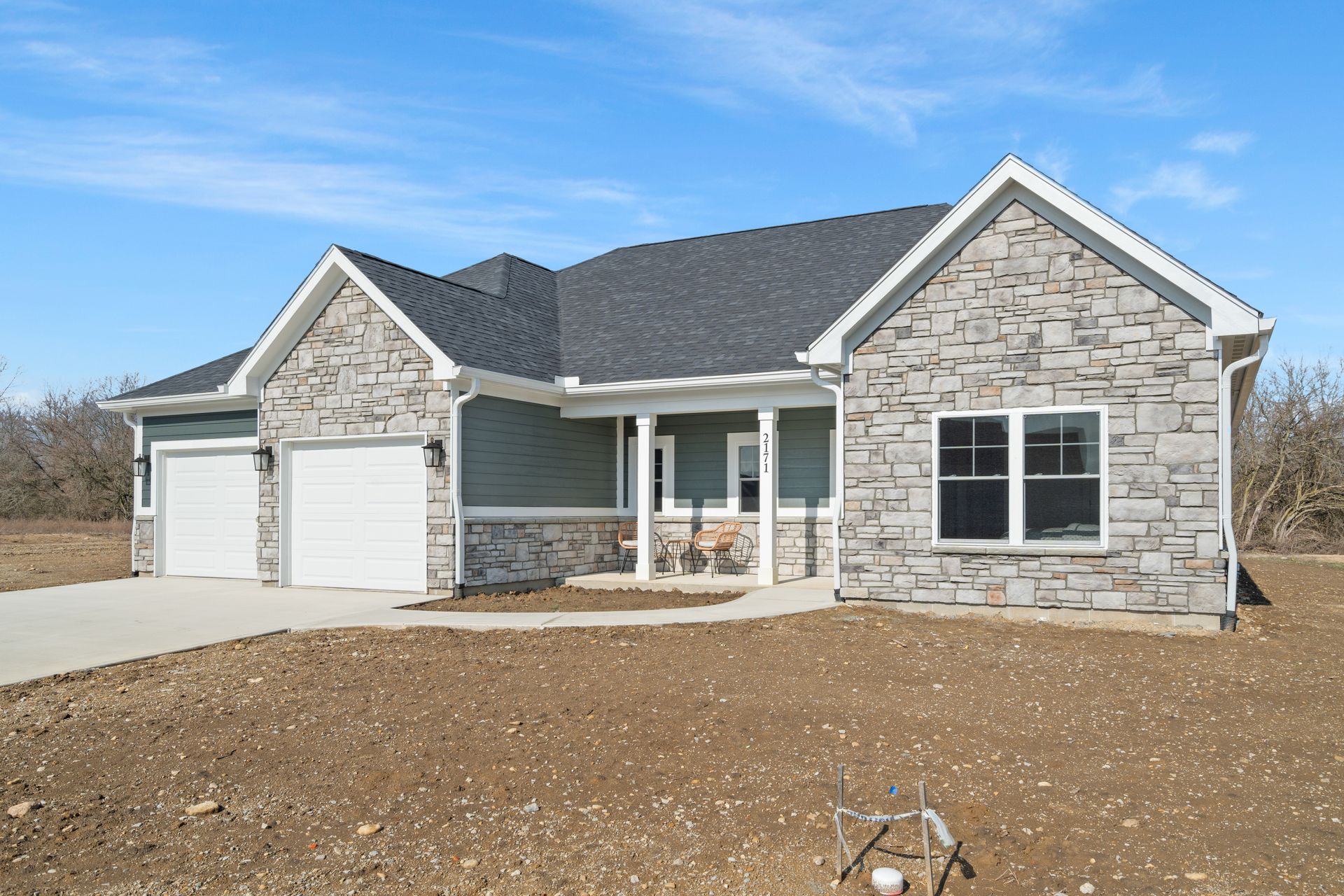 A house with a stone facade and a gray roof is sitting on top of a dirt field.