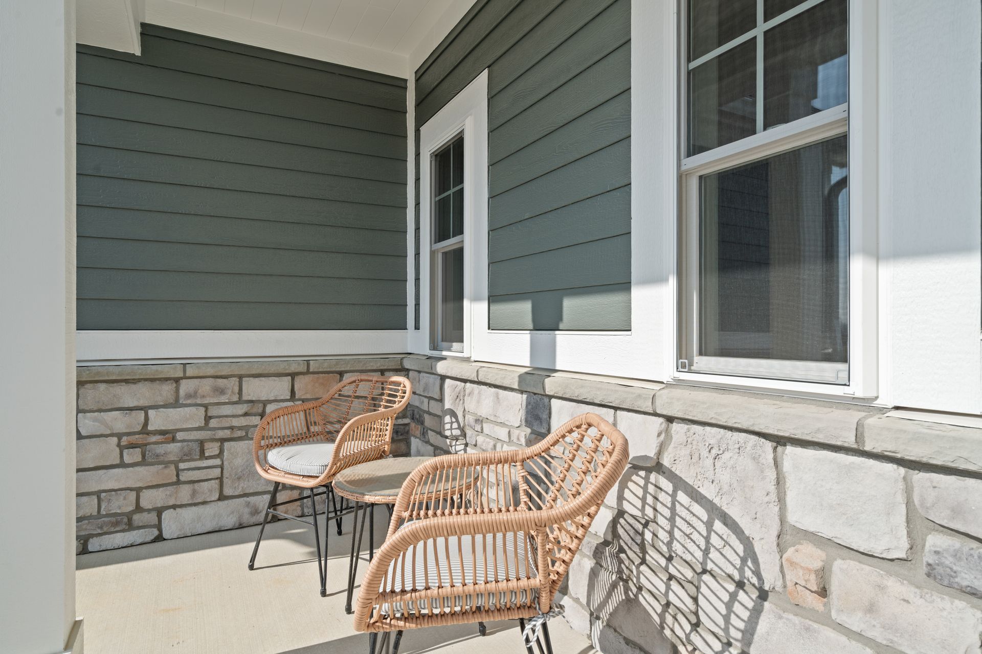 A porch with wicker chairs and a table in front of a house.