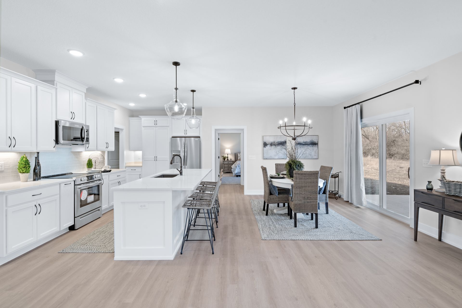 A kitchen and dining room in a new home with white cabinets and hardwood floors.