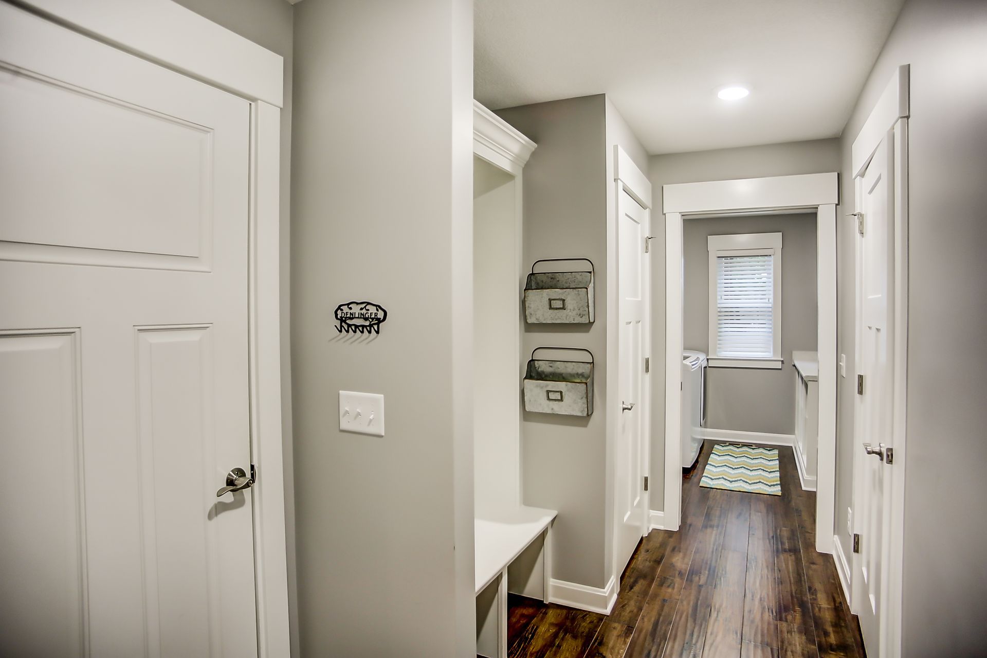A hallway with hardwood floors and white doors leading to a laundry room.