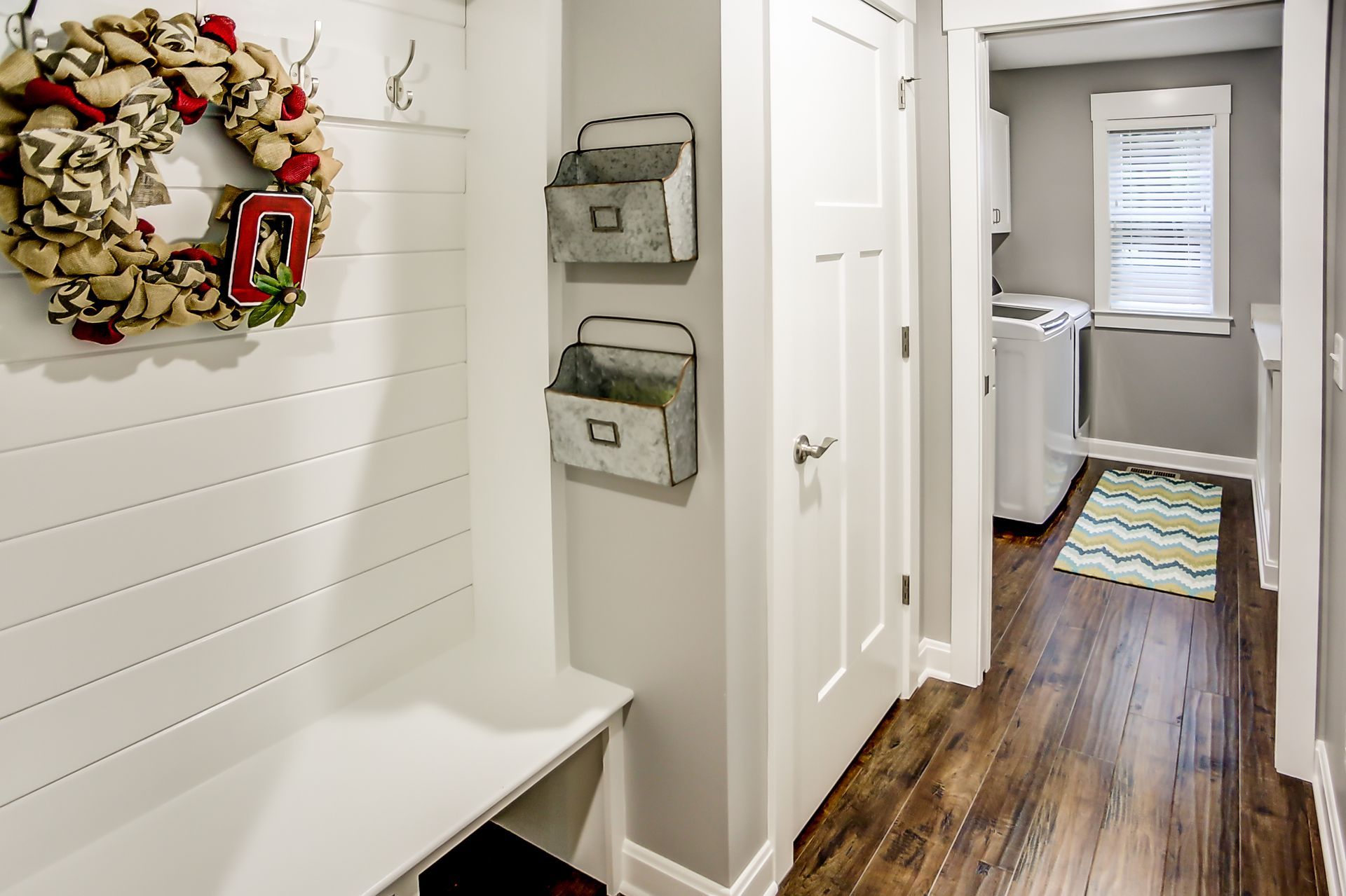A hallway with a bench and a wreath on the wall leading to a laundry room.