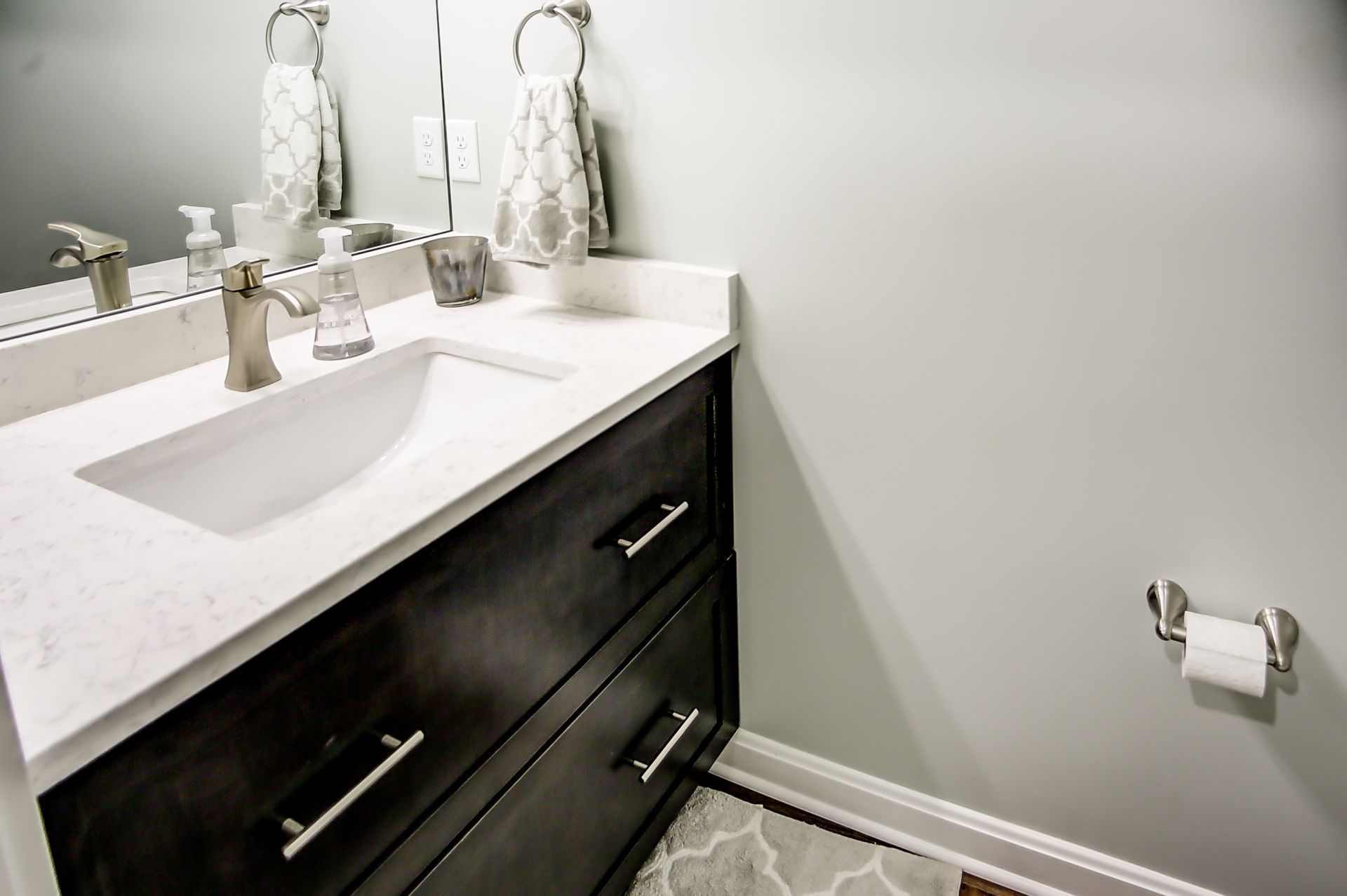 A bathroom with a sink , mirror and toilet paper.