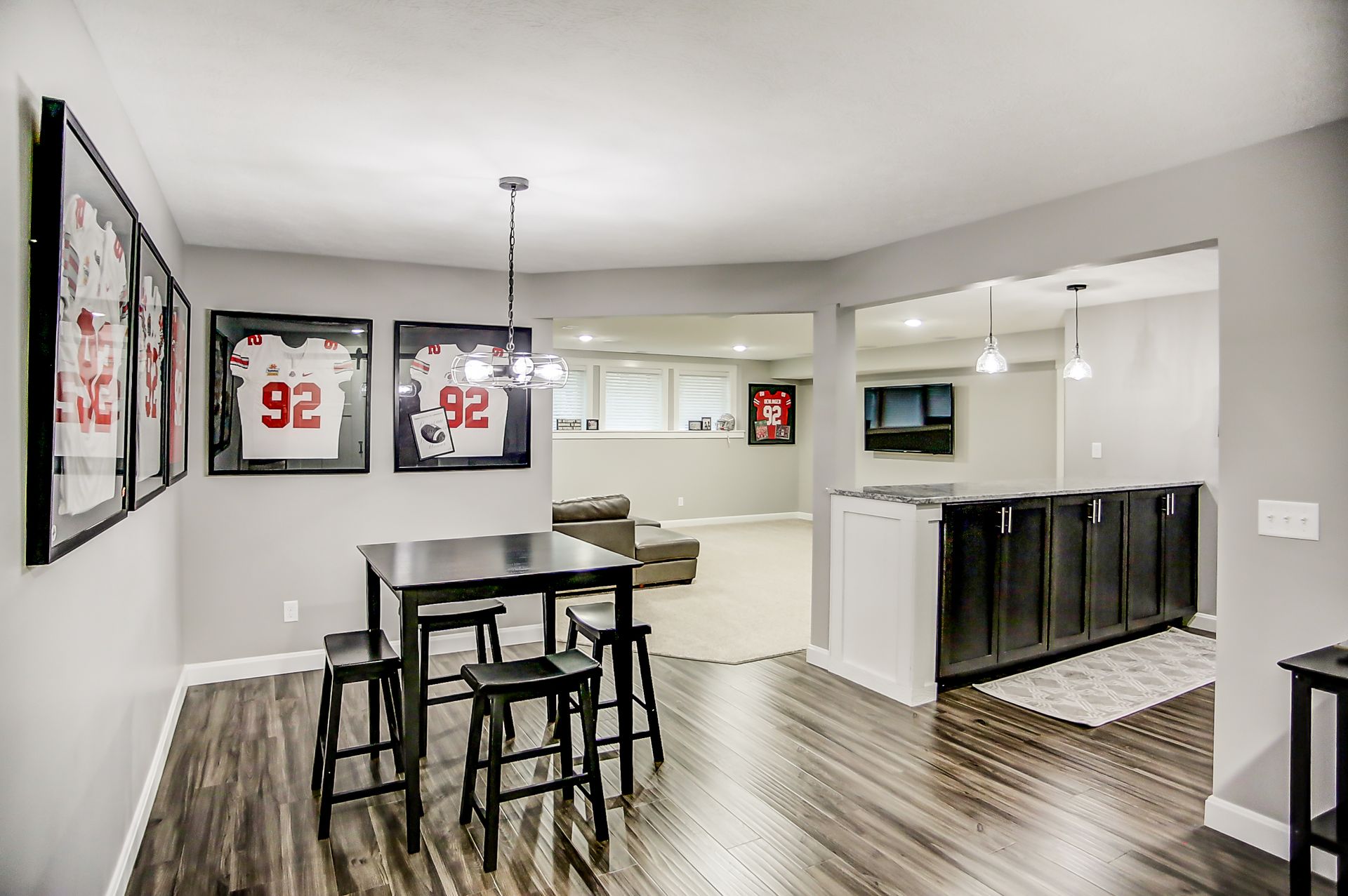 A basement with a table and stools and jerseys on the wall.