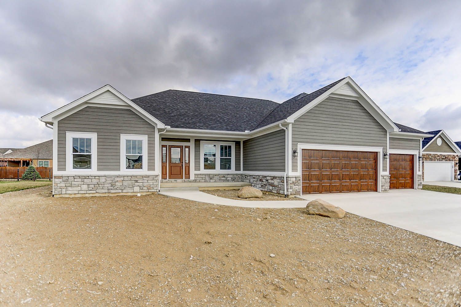 A large gray house with a brown garage door is sitting on top of a dirt field.
