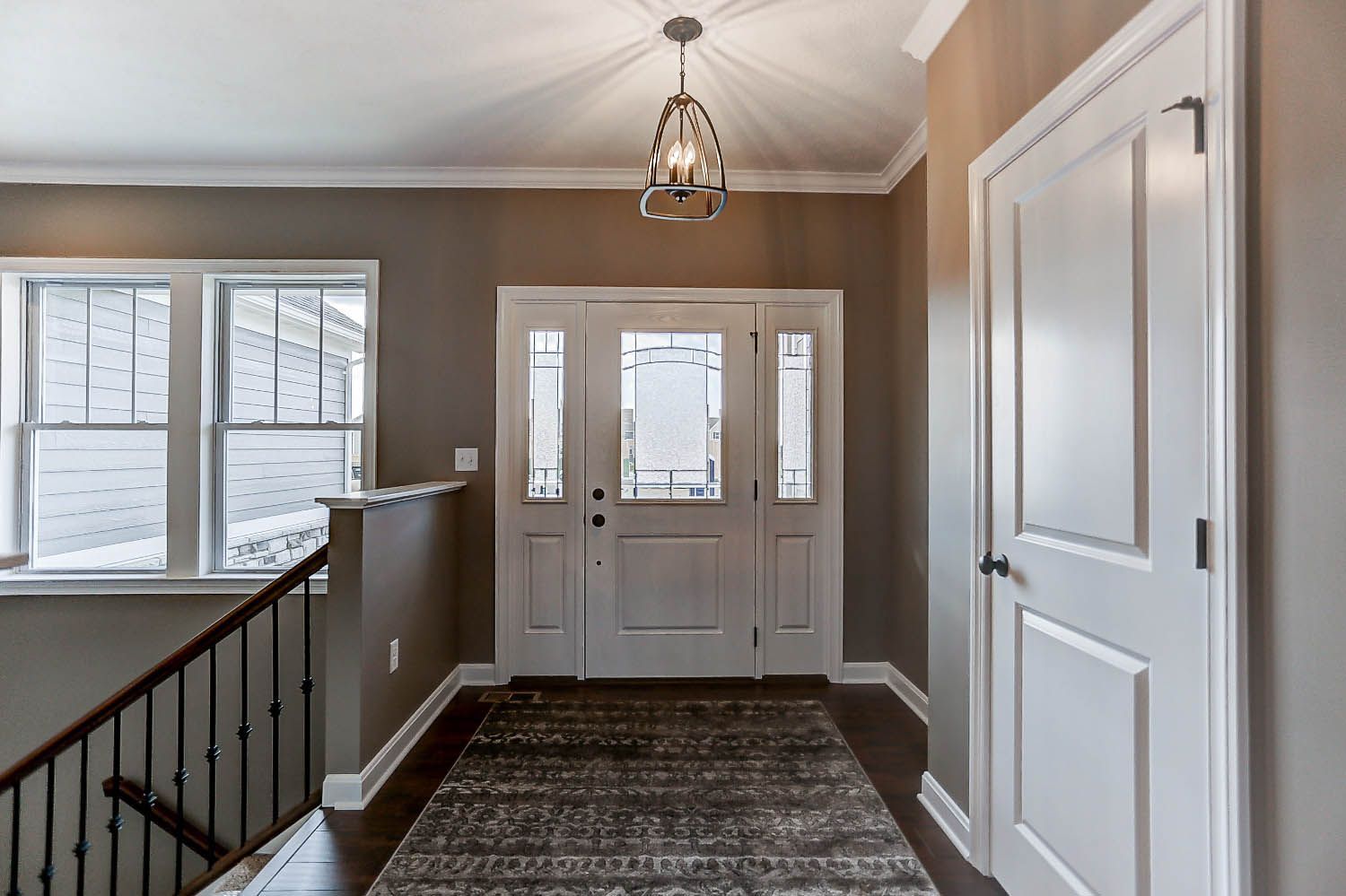A hallway in a house with a white door and a chandelier hanging from the ceiling.