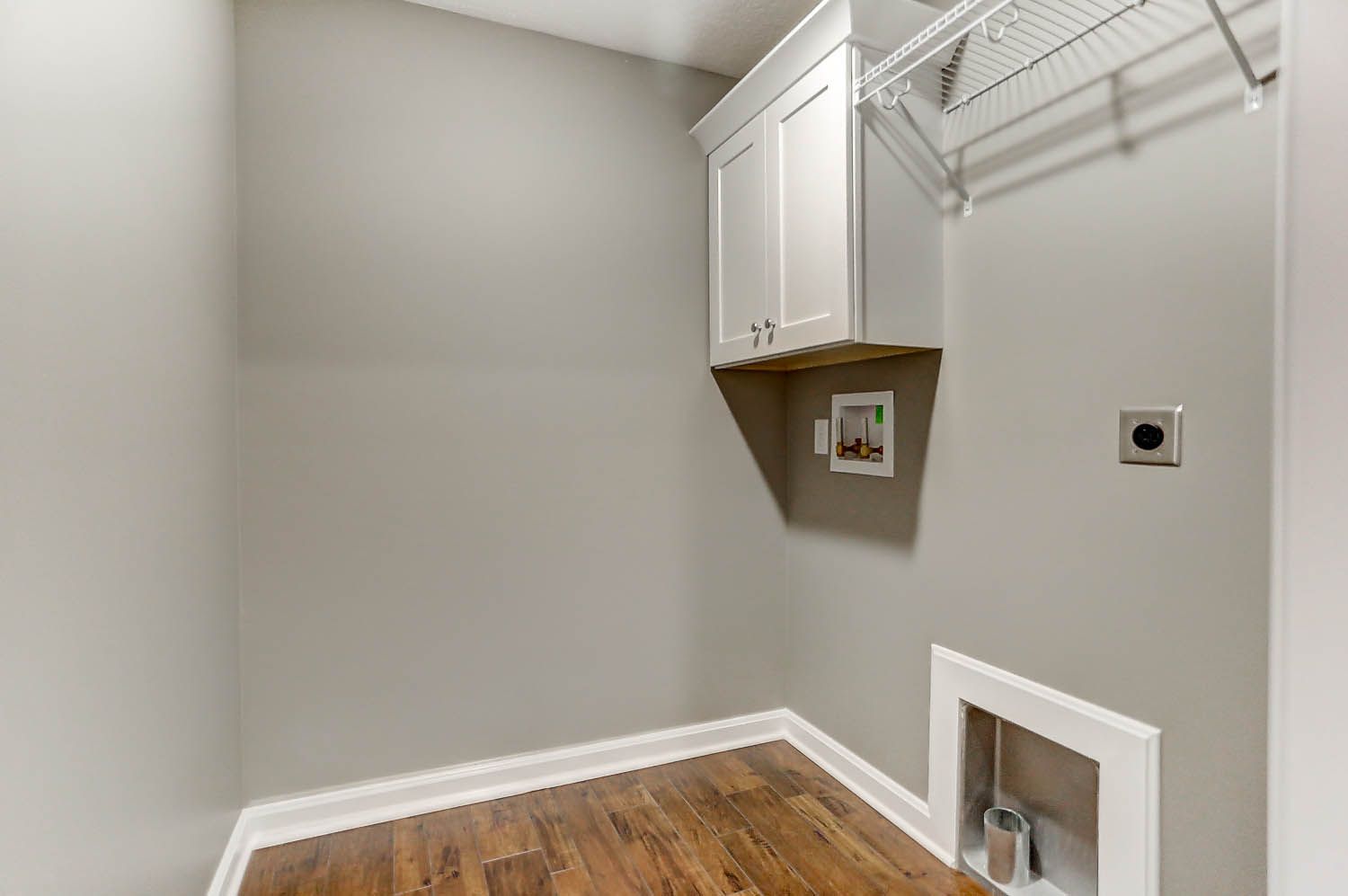 A laundry room with hardwood floors and white cabinets.