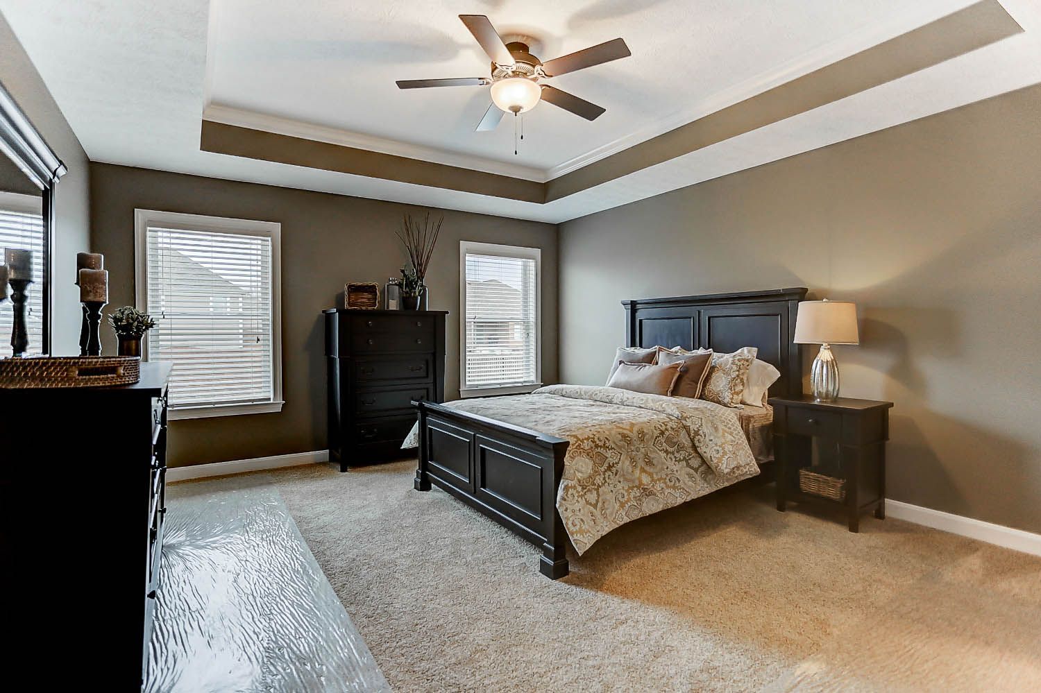 A bedroom with a bed , dresser , nightstand , mirror and ceiling fan.