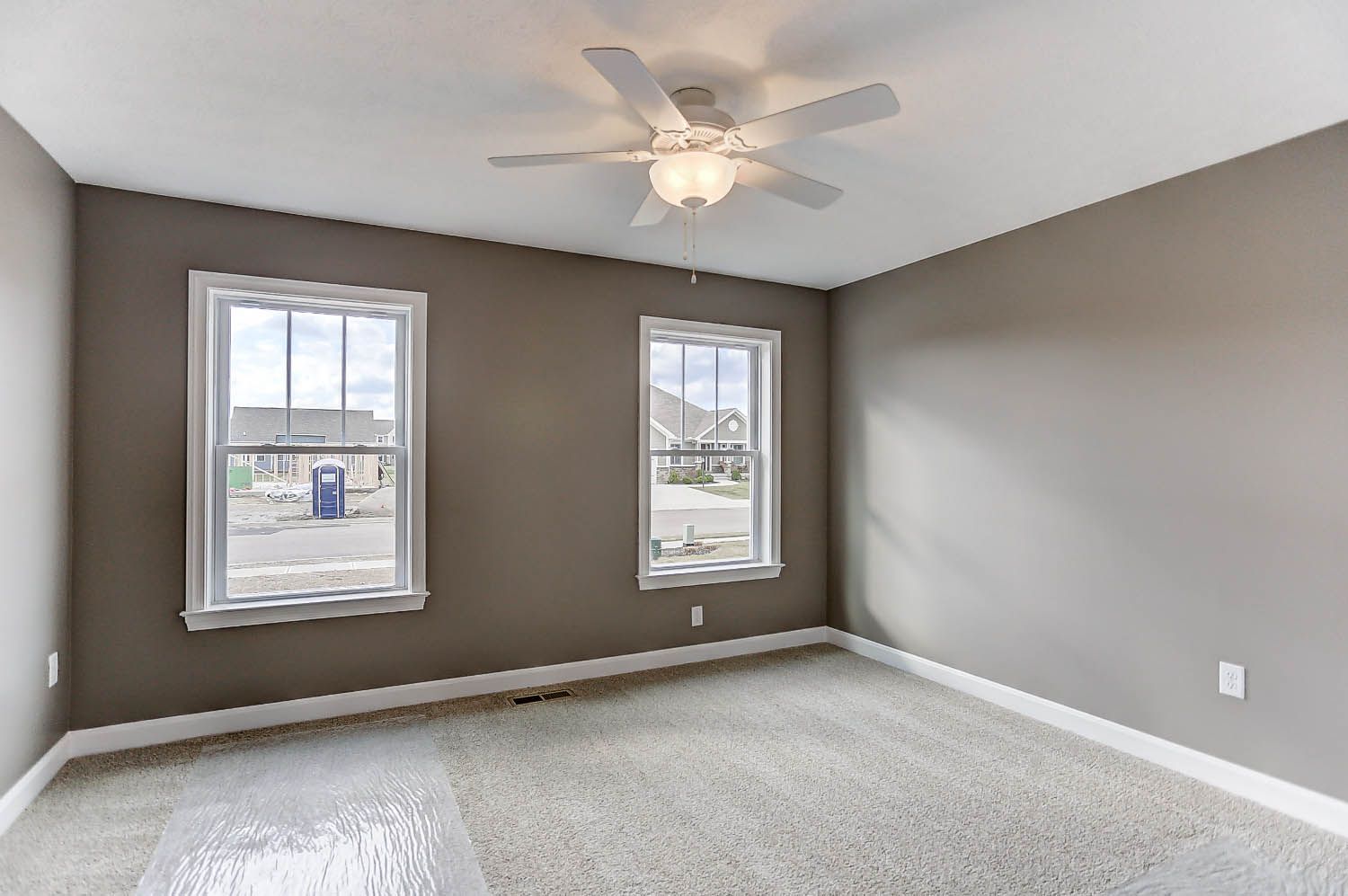 An empty bedroom with two windows and a ceiling fan.