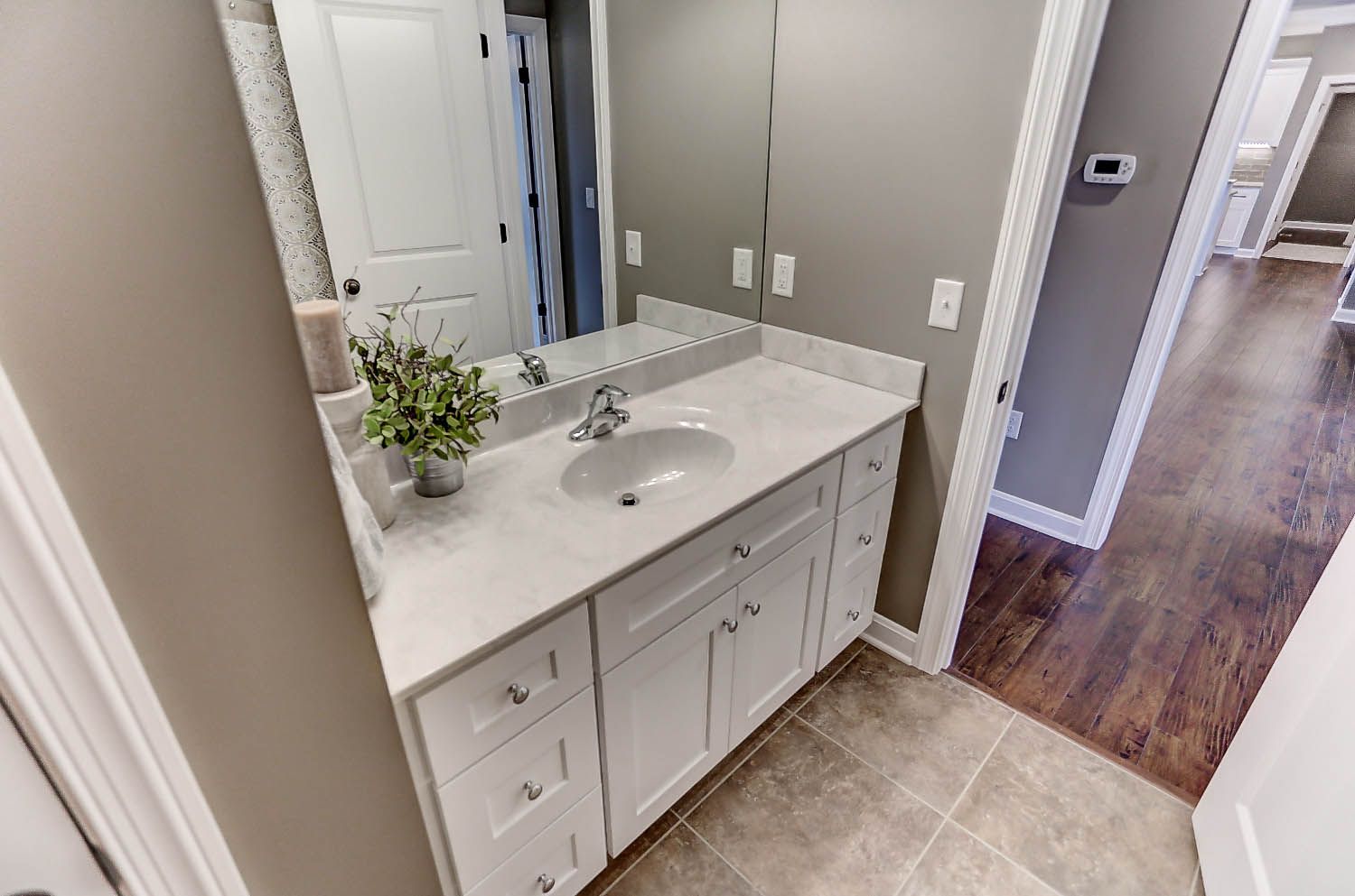 A bathroom with a sink , mirror , cabinets and hardwood floors.