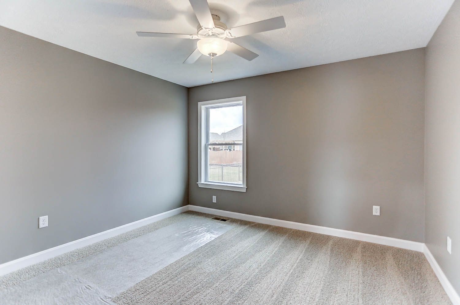 An empty bedroom with a ceiling fan and a window.