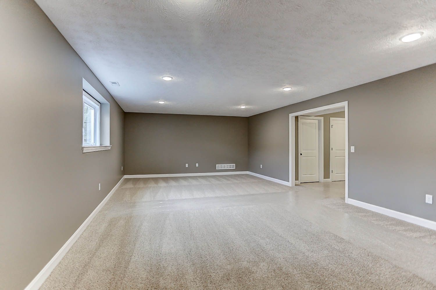 An empty basement with a carpeted floor and gray walls.