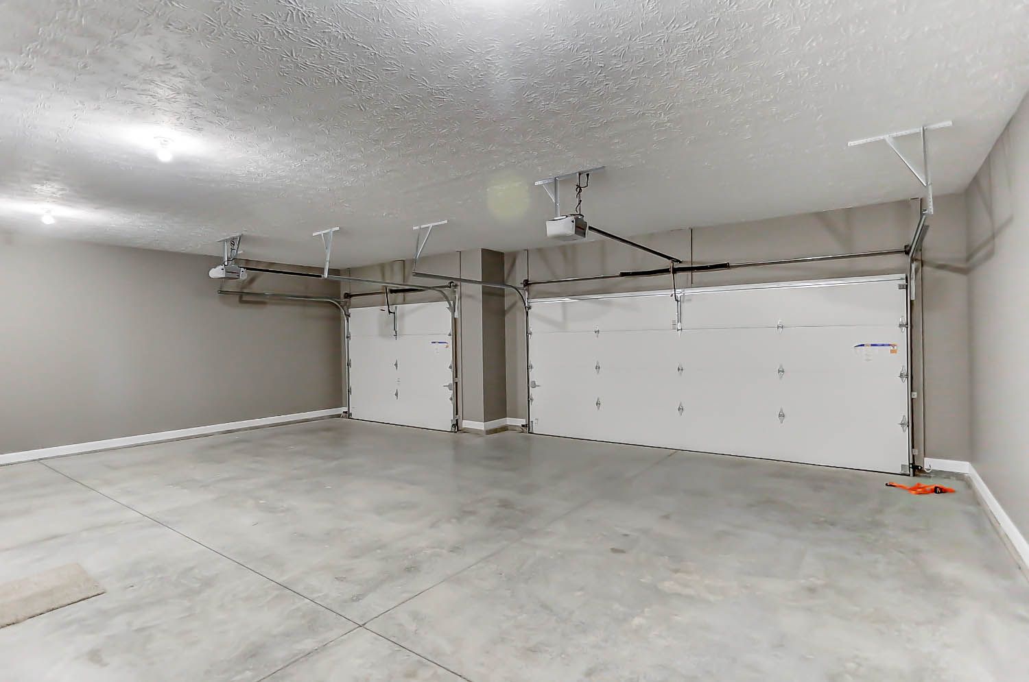 An empty garage with two white garage doors and a ceiling fan.